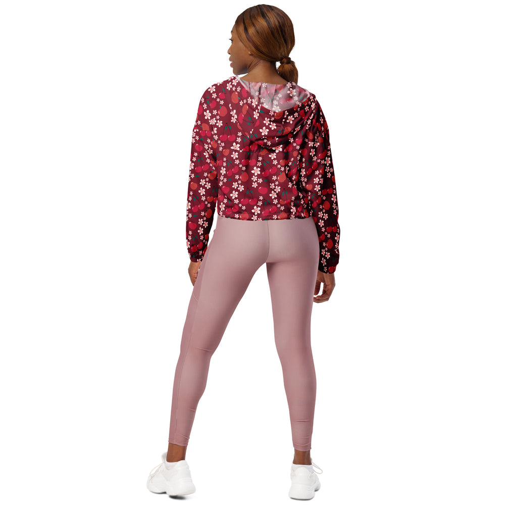 A woman wearing a maroon and white floral print cropped windbreaker with an adjustable hood and pockets