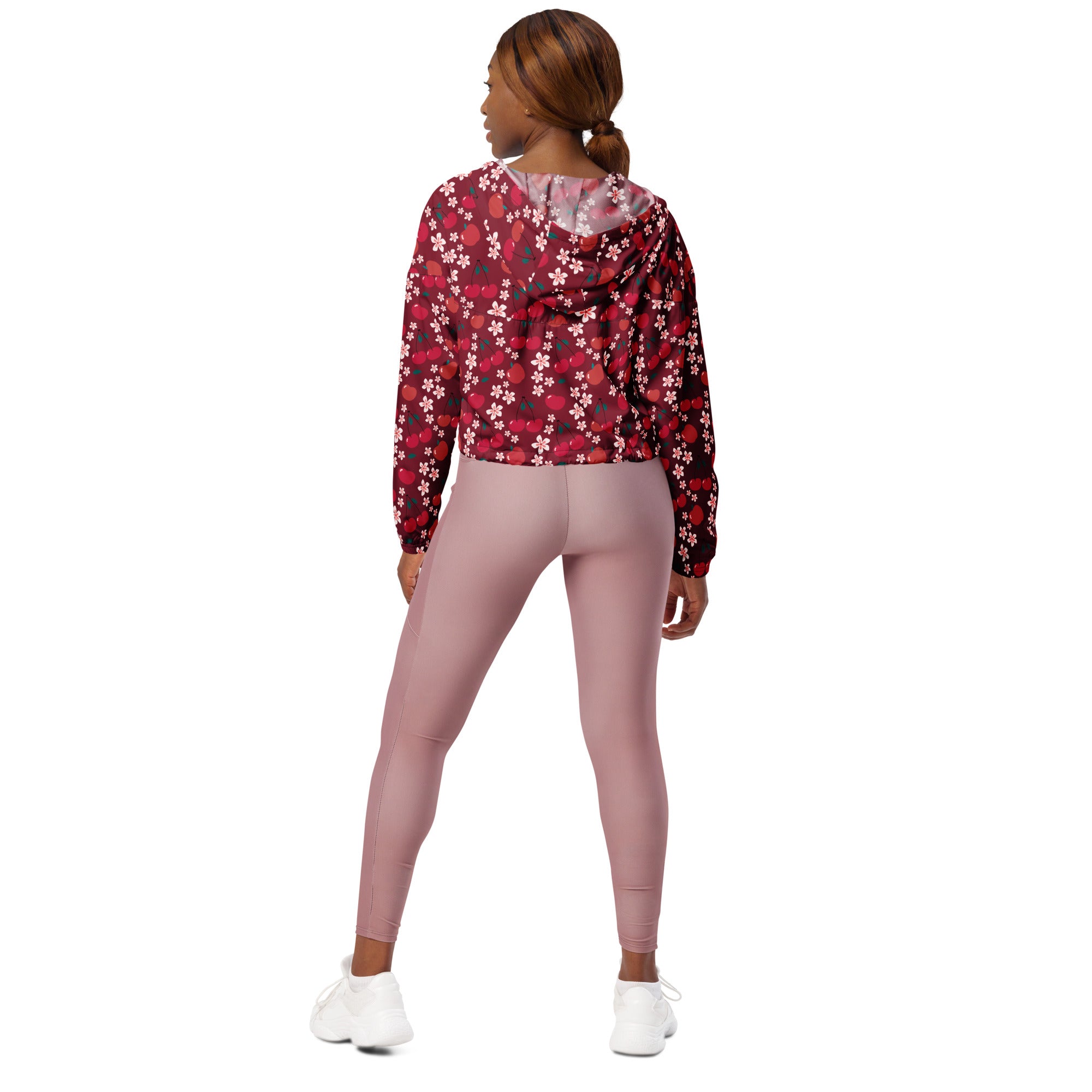 A woman wearing a maroon and white floral print cropped windbreaker with an adjustable hood and pockets