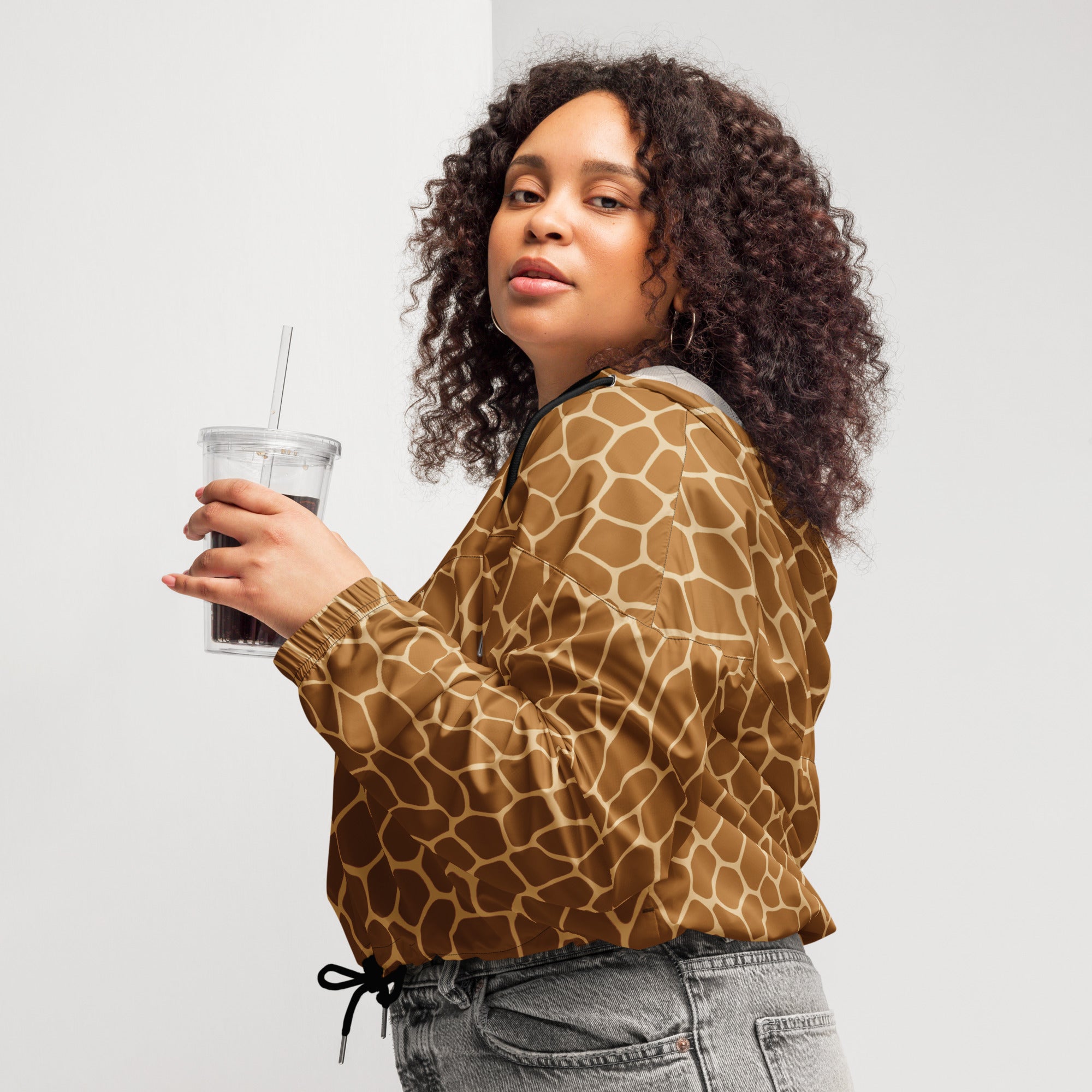 A woman wearing a brown and tan giraffe print cropped windbreaker with black drawstrings and adjustable hood