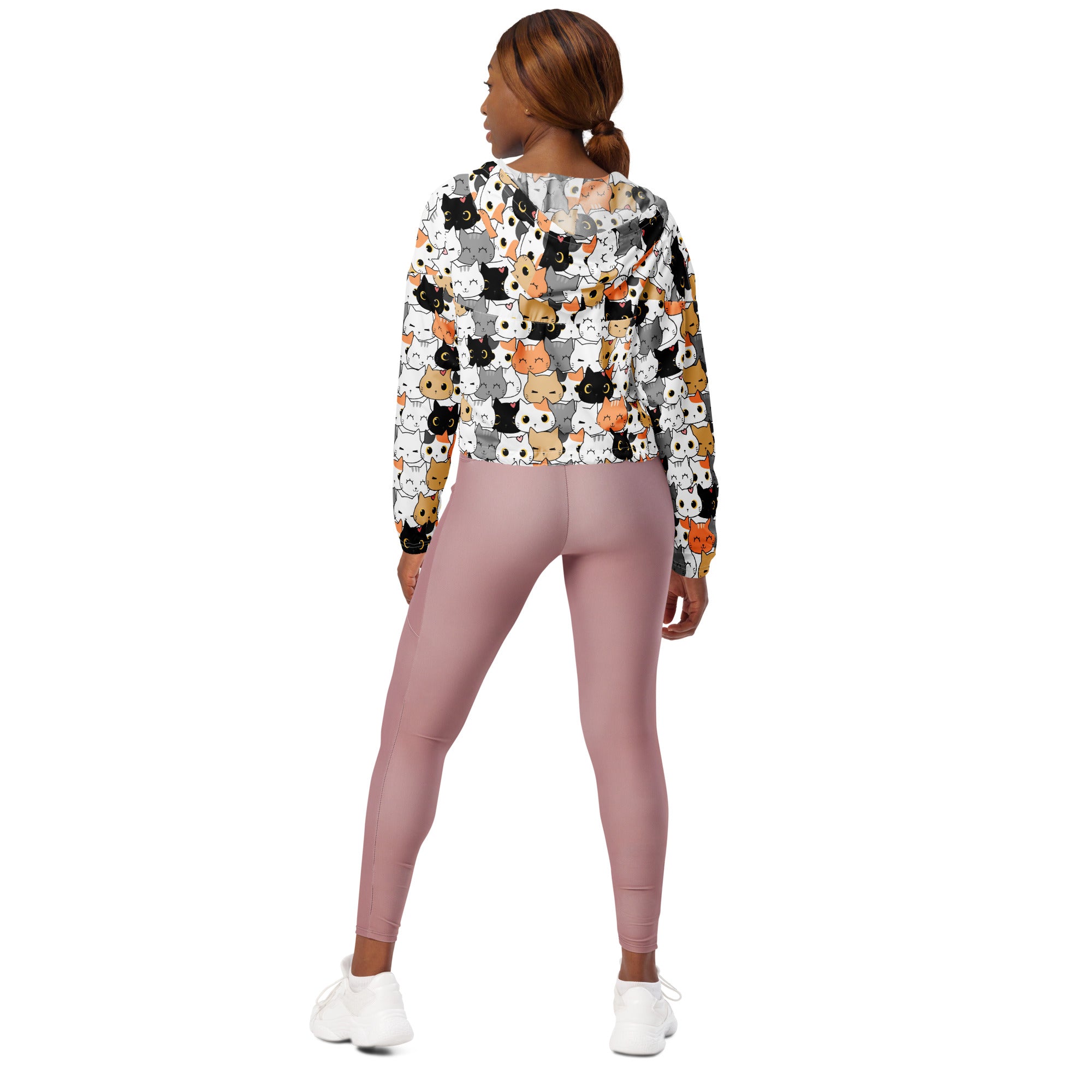A woman wears a lightweight water resistant women’s cat face cropped windbreaker with colorful cartoon cats and an adjustable hood