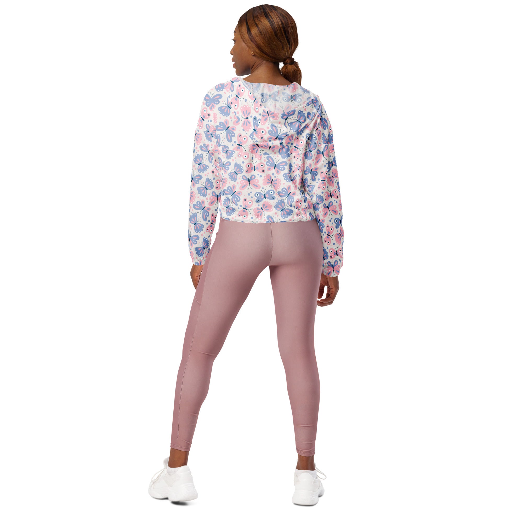 A woman wears a women’s pastel butterfly cropped windbreaker with adjustable hood and pockets in soft pink and lavender hues