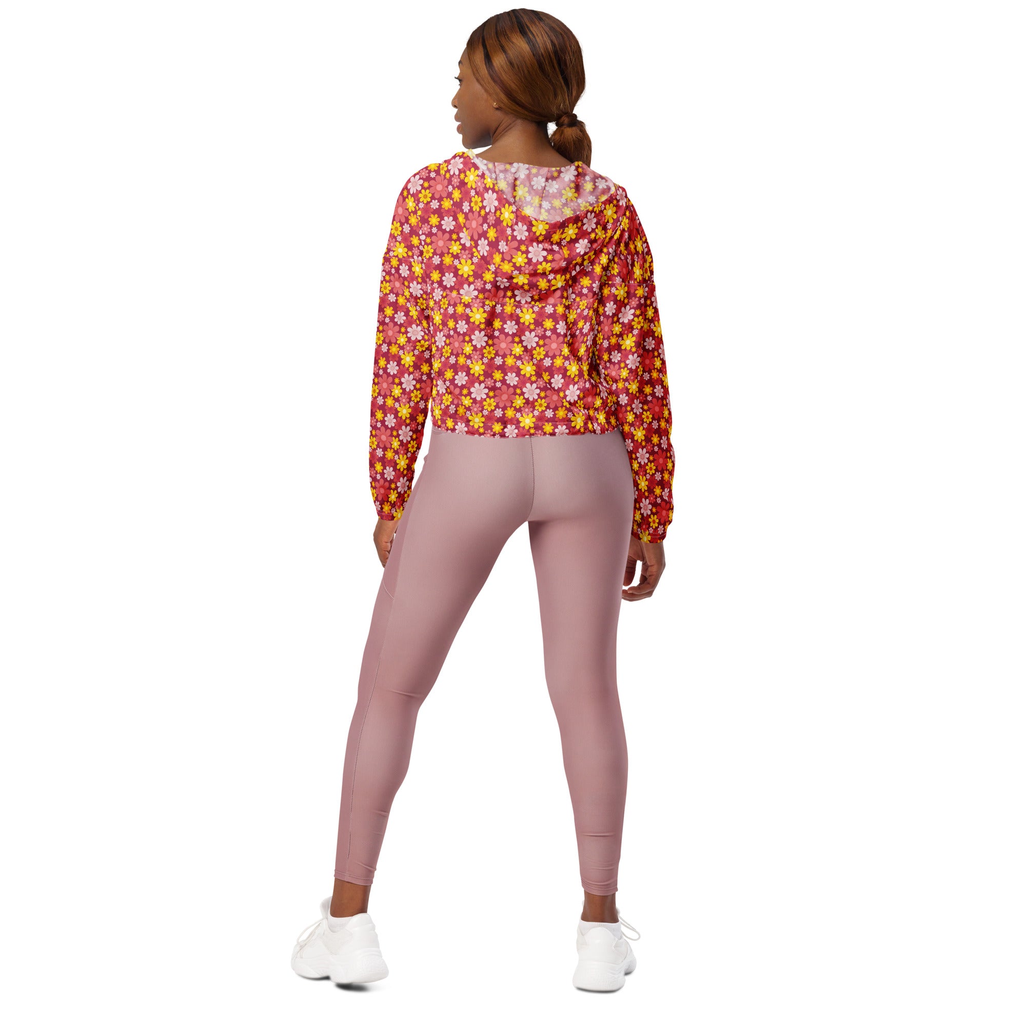 A woman wears a vibrant red floral cropped windbreaker with adjustable hood and pockets over mauve leggings