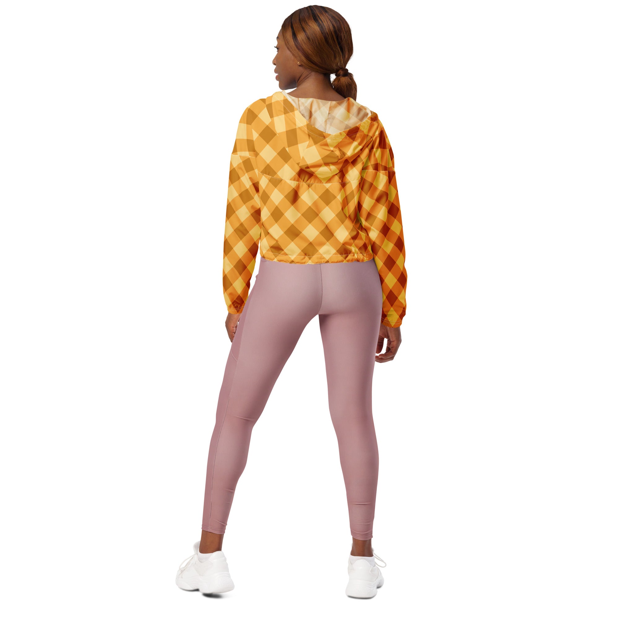 A woman wearing a women’s orange gingham cropped windbreaker with adjustable hood paired with mauve leggings