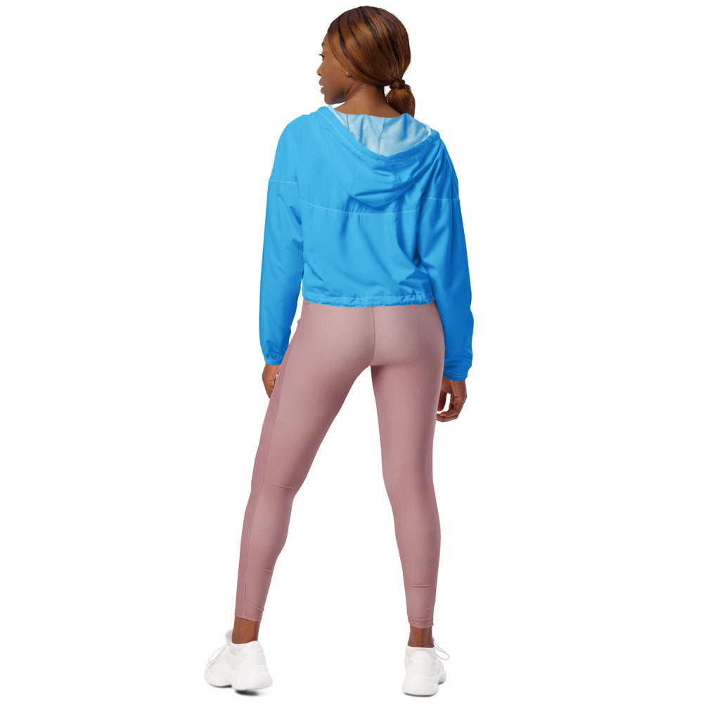 A woman wearing a women’s sky blue cropped windbreaker with adjustable hood and pockets paired with mauve leggings