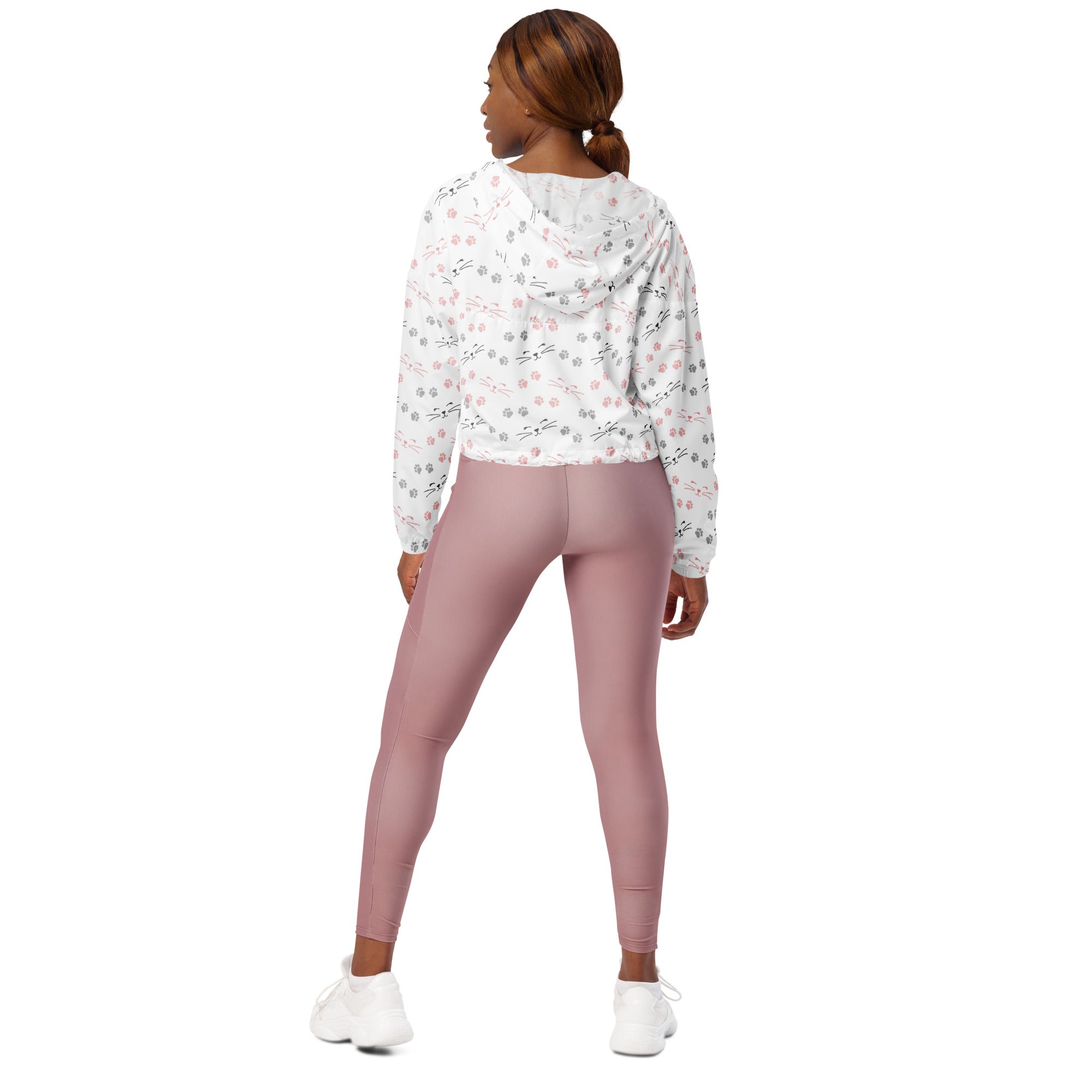 A woman wears a white floral patterned cropped windbreaker with adjustable hood and pockets paired with dusty rose leggings