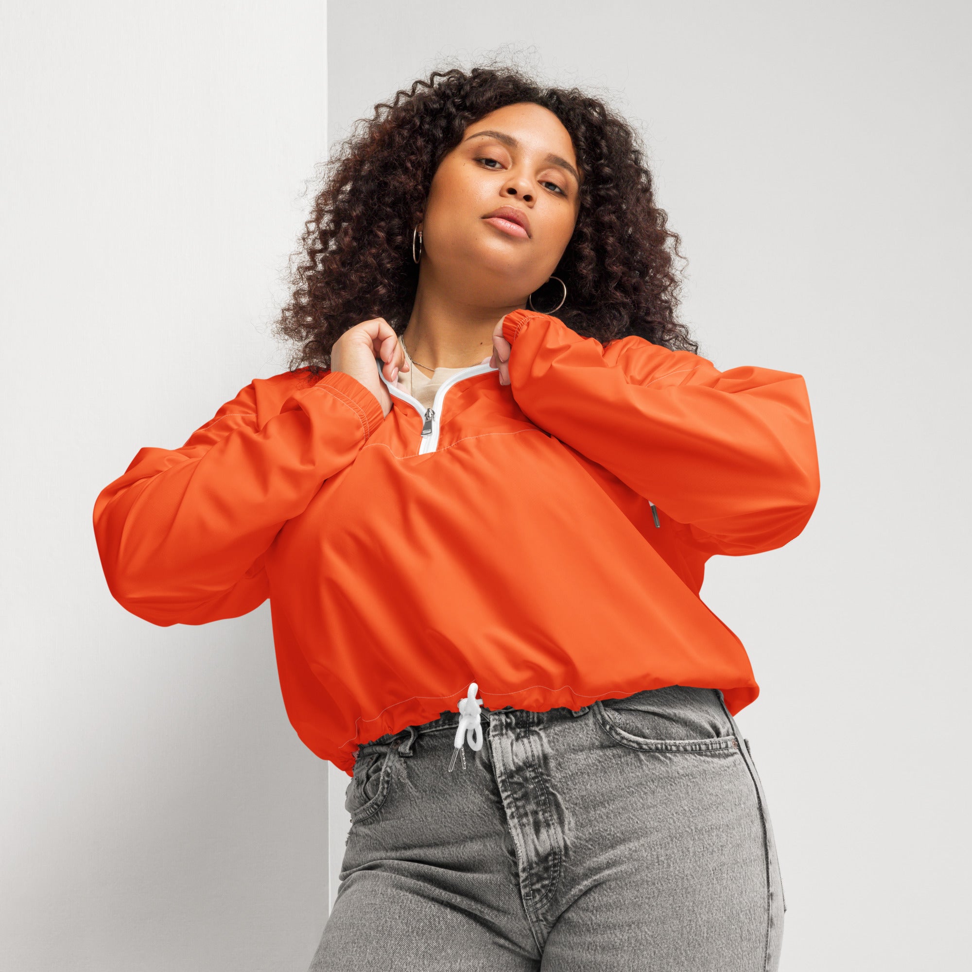 Woman wearing a vibrant orange cropped puffer jacket with white zipper and drawstring hem, lightweight and water resistant