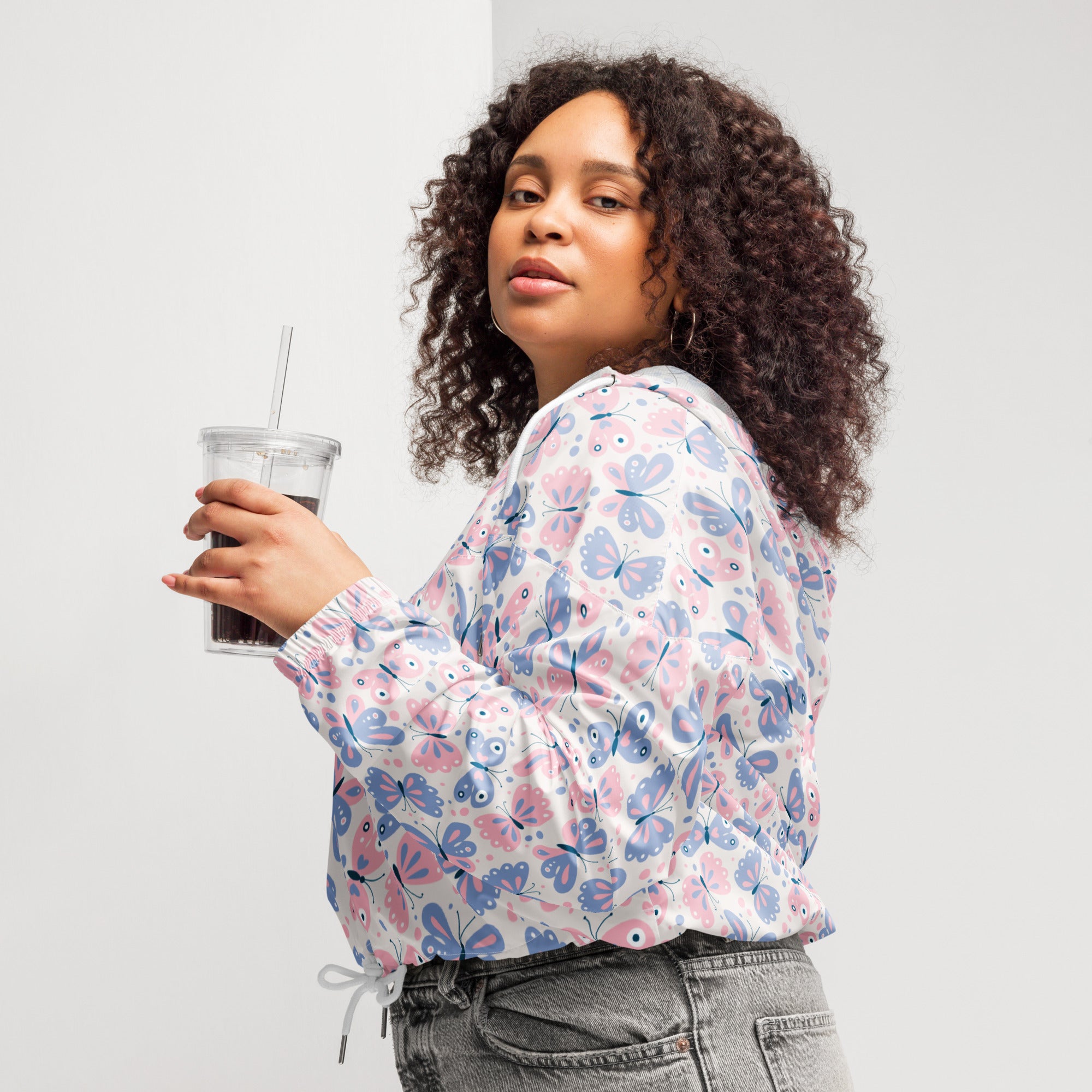 A woman wears a white pastel butterfly cropped windbreaker with pink and blue prints and an adjustable hood