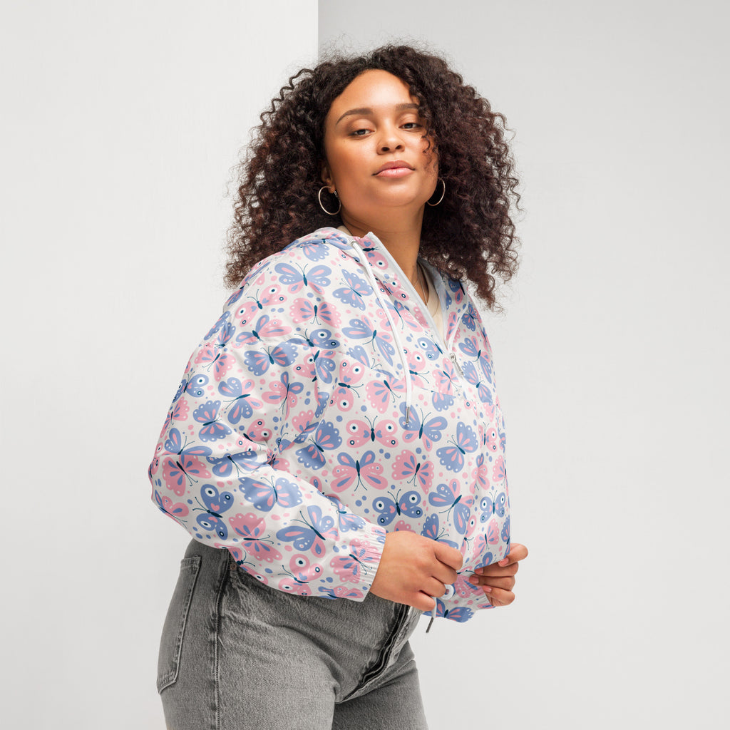 A woman wears a lightweight white bomber jacket with pink and blue butterfly prints and an adjustable hood