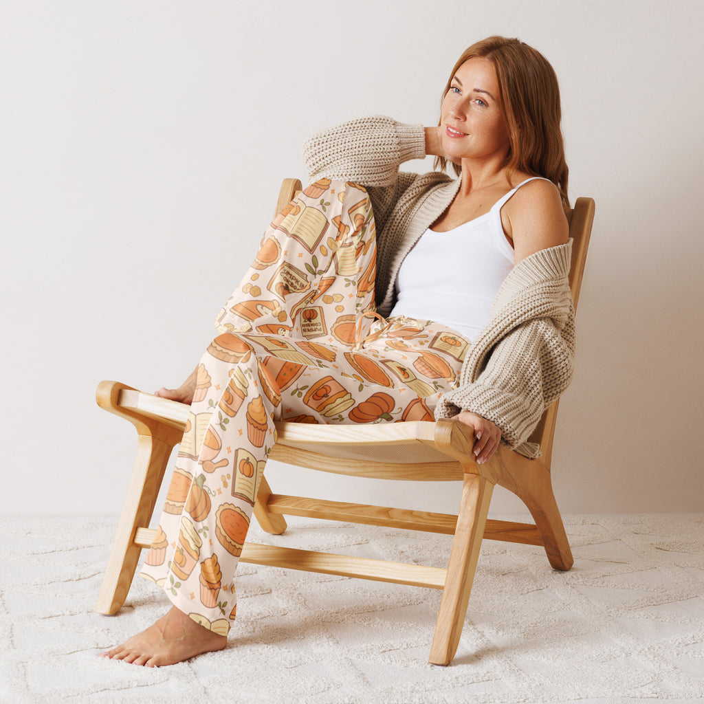 Woman wearing lightweight beige knit cardigan and pumpkin pie themed pajama pants with pastry illustrations on cream background