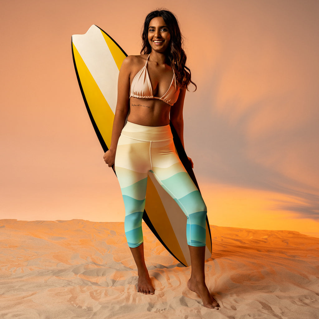 A woman stands barefoot on sand wearing women’s coastal gradient buttery soft high-rise moisture-wicking yoga capri leggings