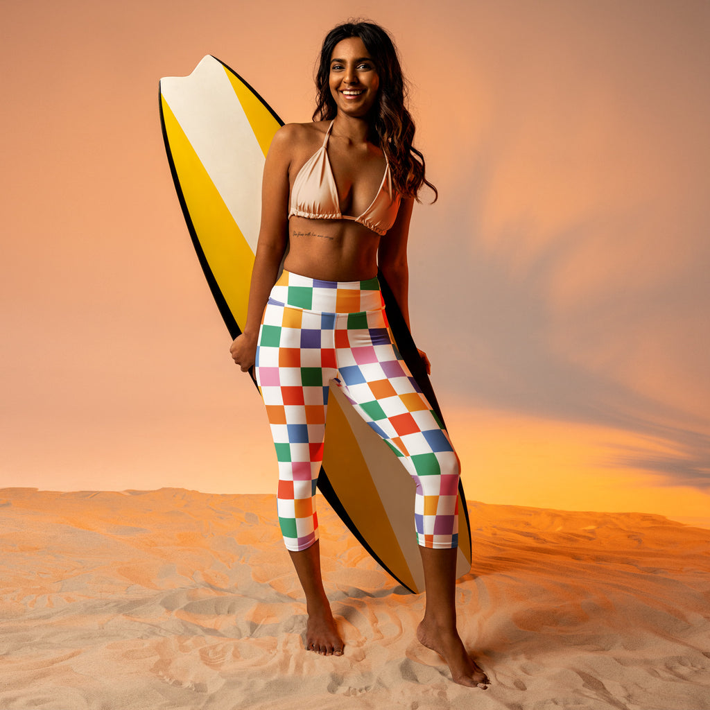 Woman wearing colorful checkered high-rise buttery soft yoga capri leggings holding yellow white and black surfboard