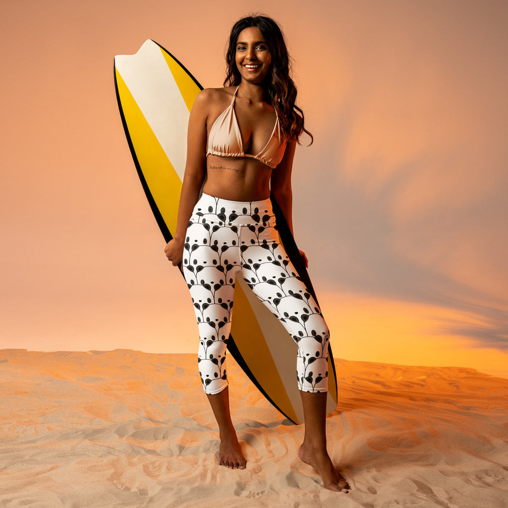 A woman wearing high-rise white panda print buttery soft yoga capri leggings holding a yellow surfboard