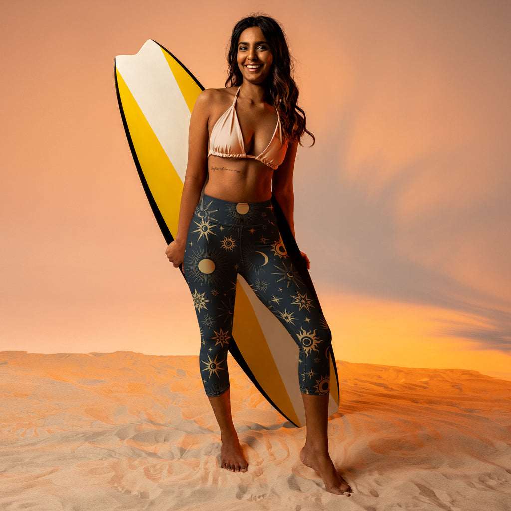 A woman wearing peach bikini top and dark blue celestial sun moon buttery soft high-rise yoga capri leggings