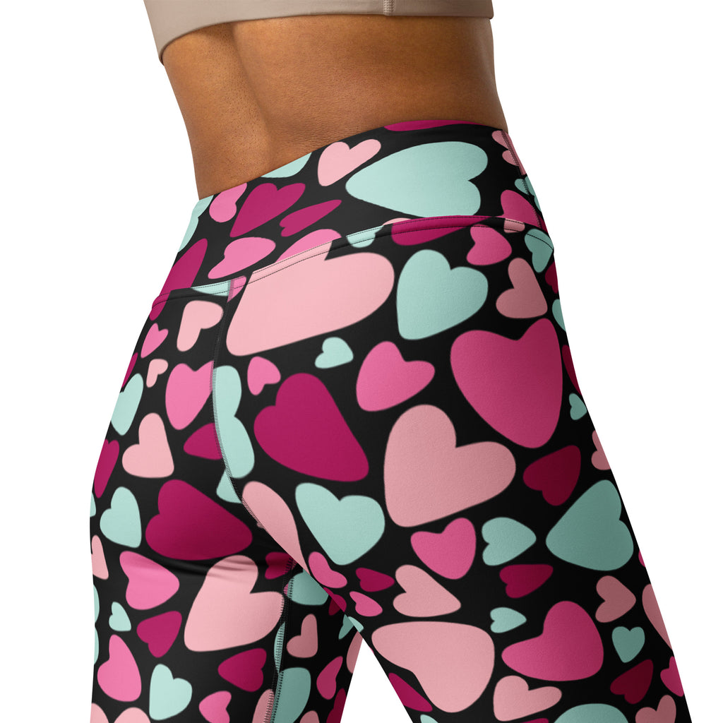 High-waisted women’s yoga leggings with a vibrant pink magenta and mint green heart pattern on black buttery soft fabric