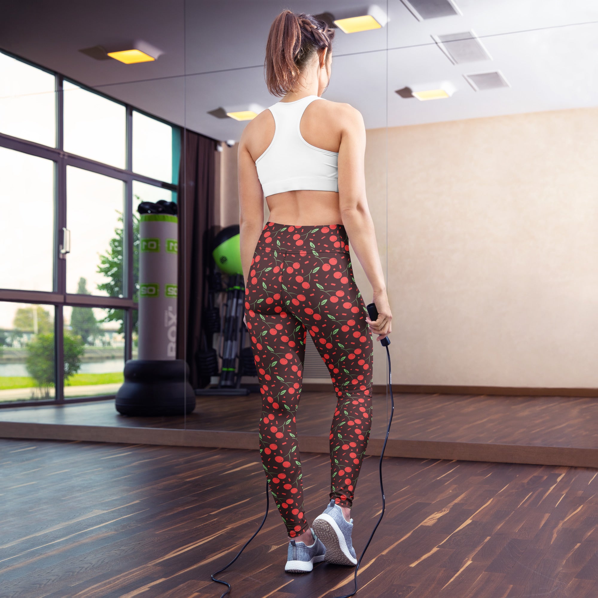 A pair of women’s dark brown high-waisted buttery soft yoga leggings with a vibrant red cherry pattern