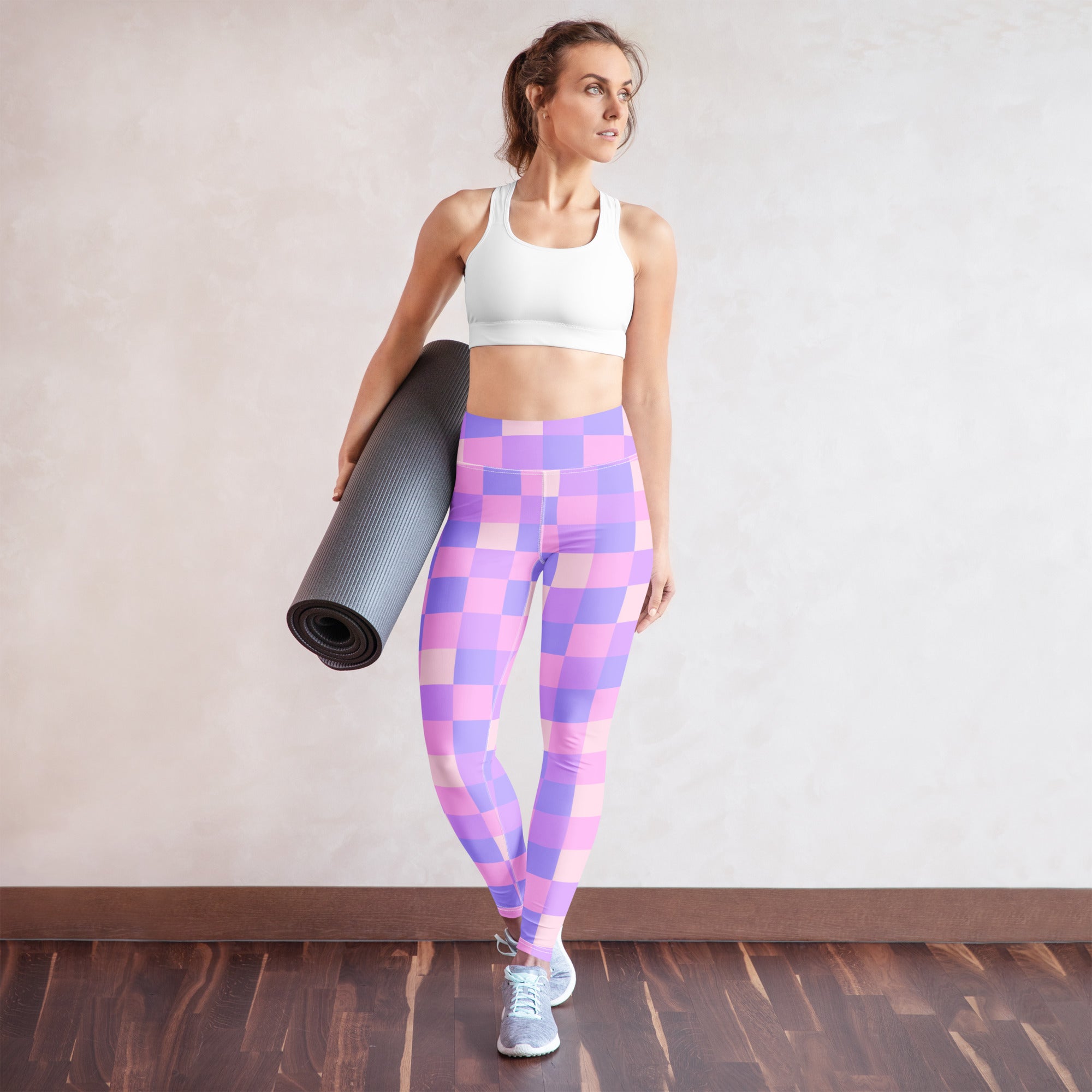 A woman wearing women’s purple checkerboard buttery soft yoga leggings with a white sports bra and gray shoes