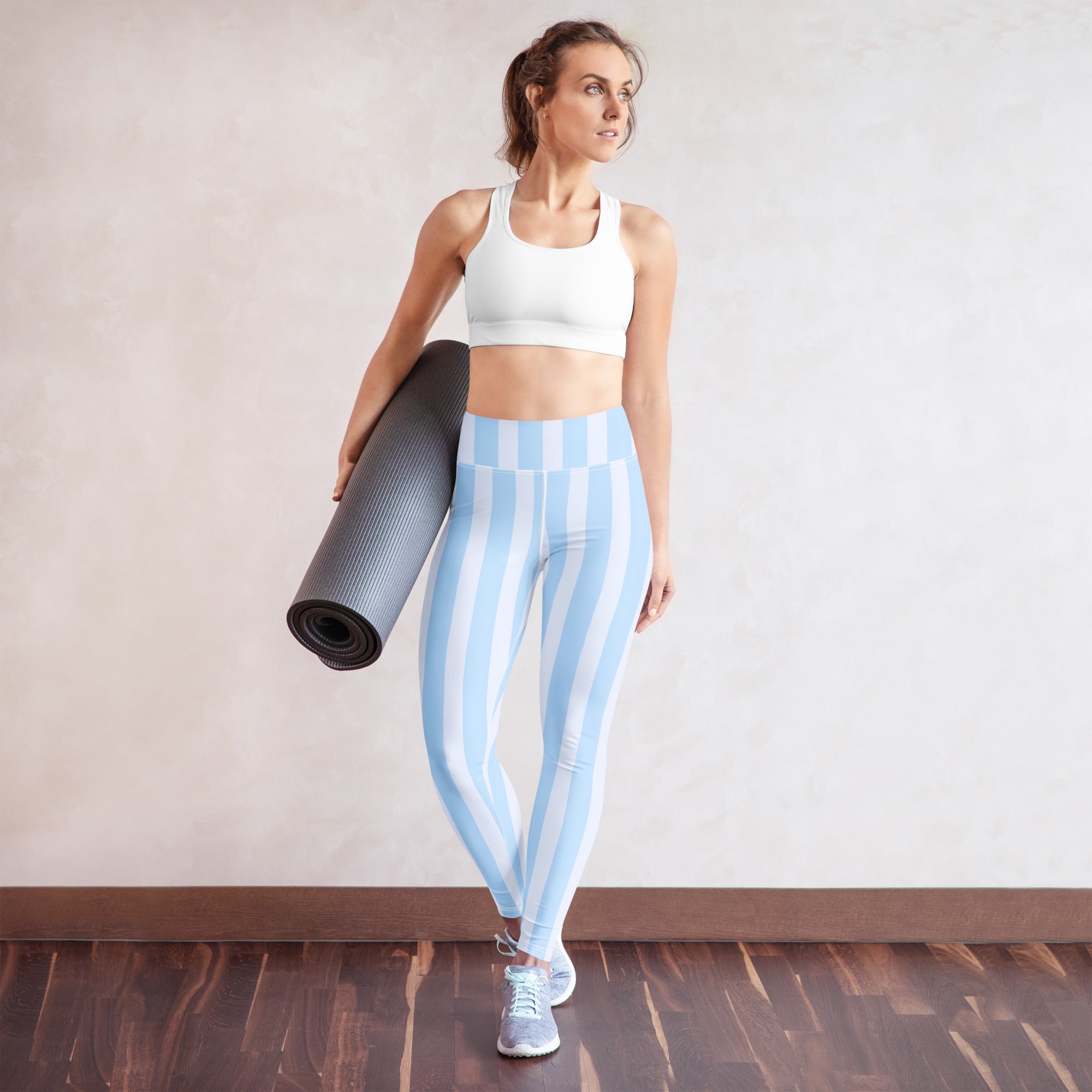 A woman wearing light blue and white striped high-waisted buttery soft yoga leggings with a white sports bra