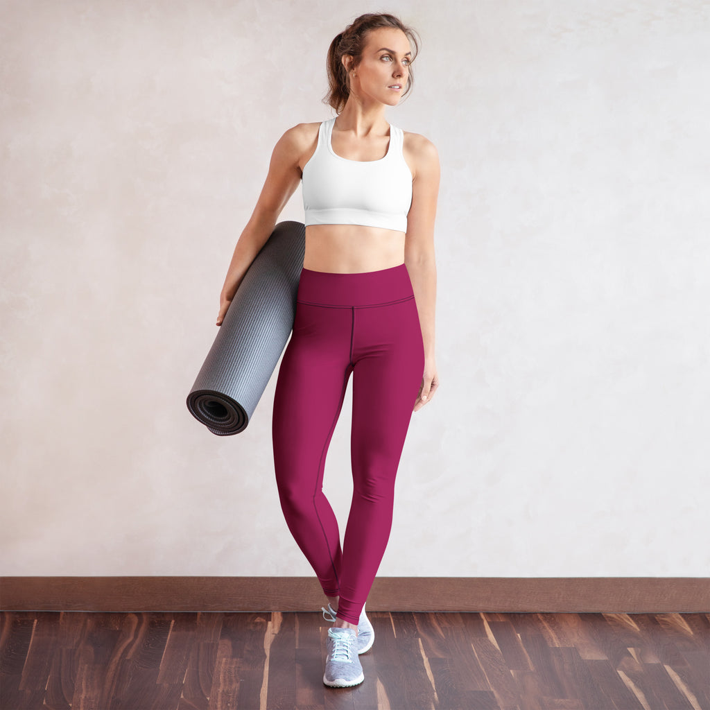 A woman wearing dark magenta buttery soft high-waisted yoga leggings holding a rolled gray yoga mat