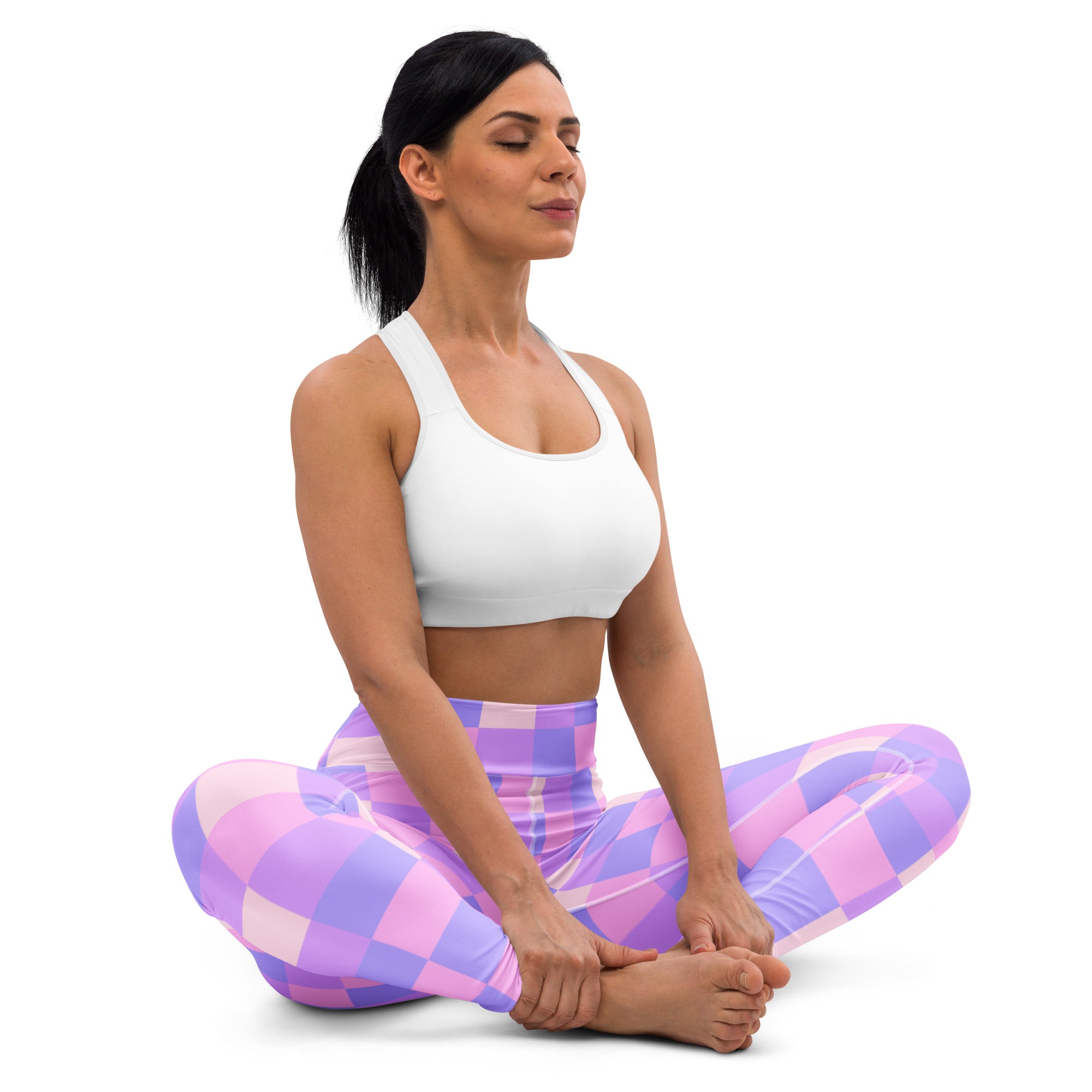 A woman seated in a yoga pose wearing purple checkerboard buttery soft leggings and a white sports bra