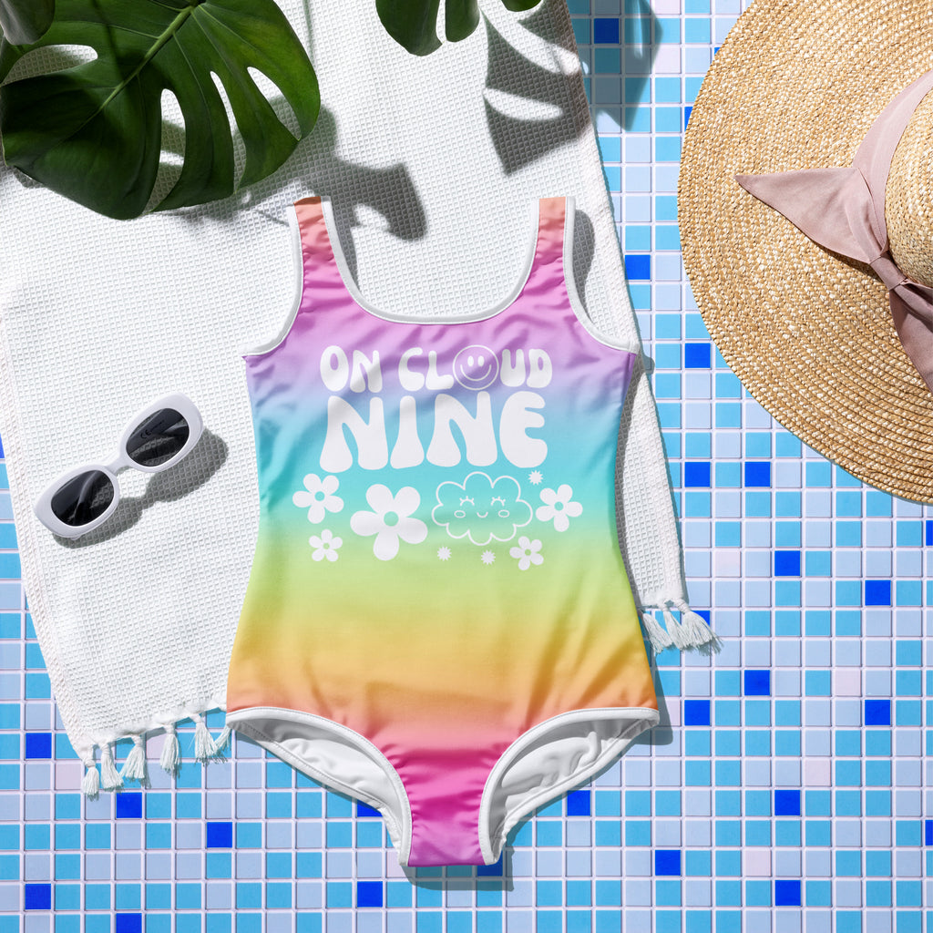 A vibrant rainbow gradient girls one-piece swimsuit with on cloud nine print and floral and cloud designs perfect for her 9th birthday