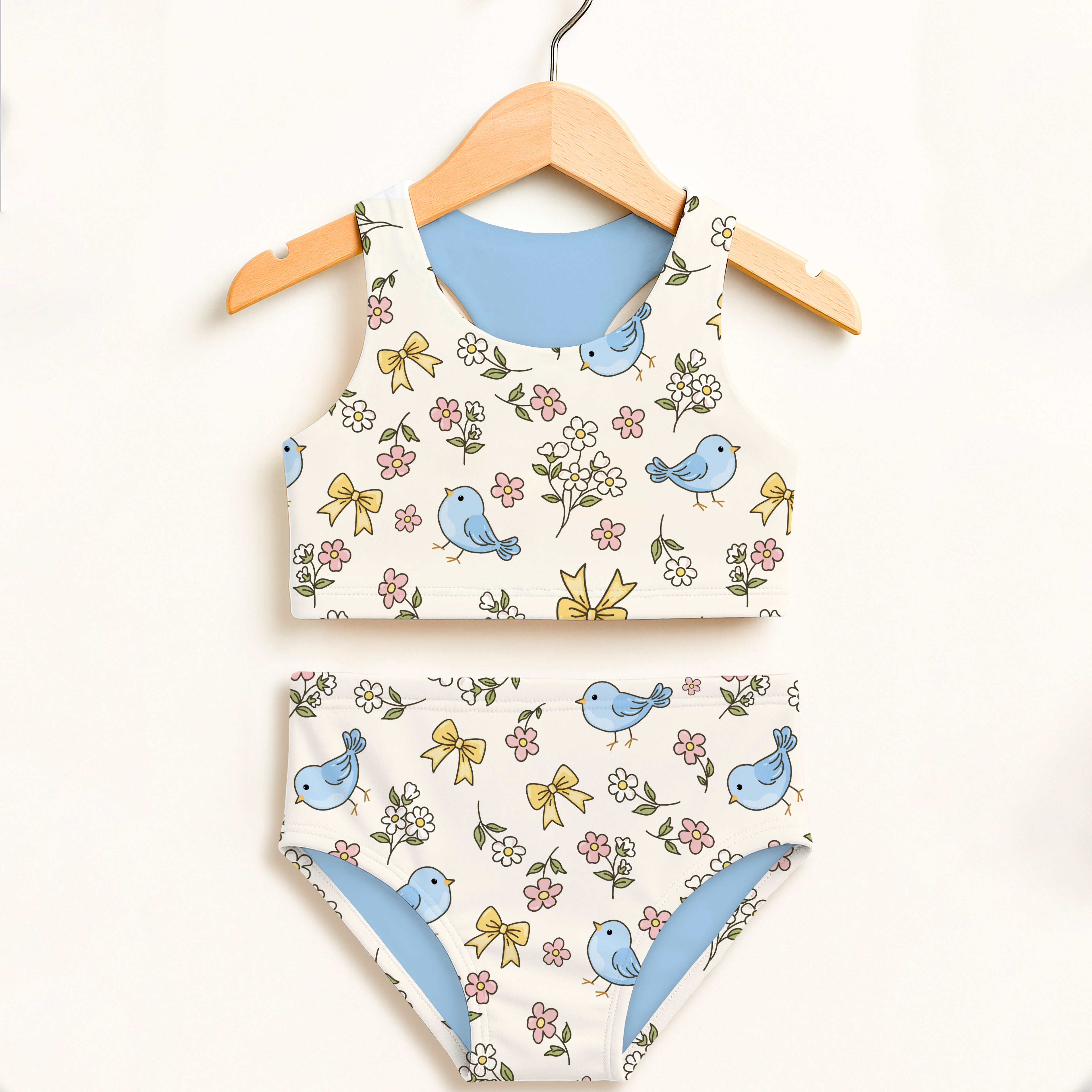 A charming white two-piece swimsuit with blue birds yellow bows and flowers featuring double layered UPF 50+ fabric
