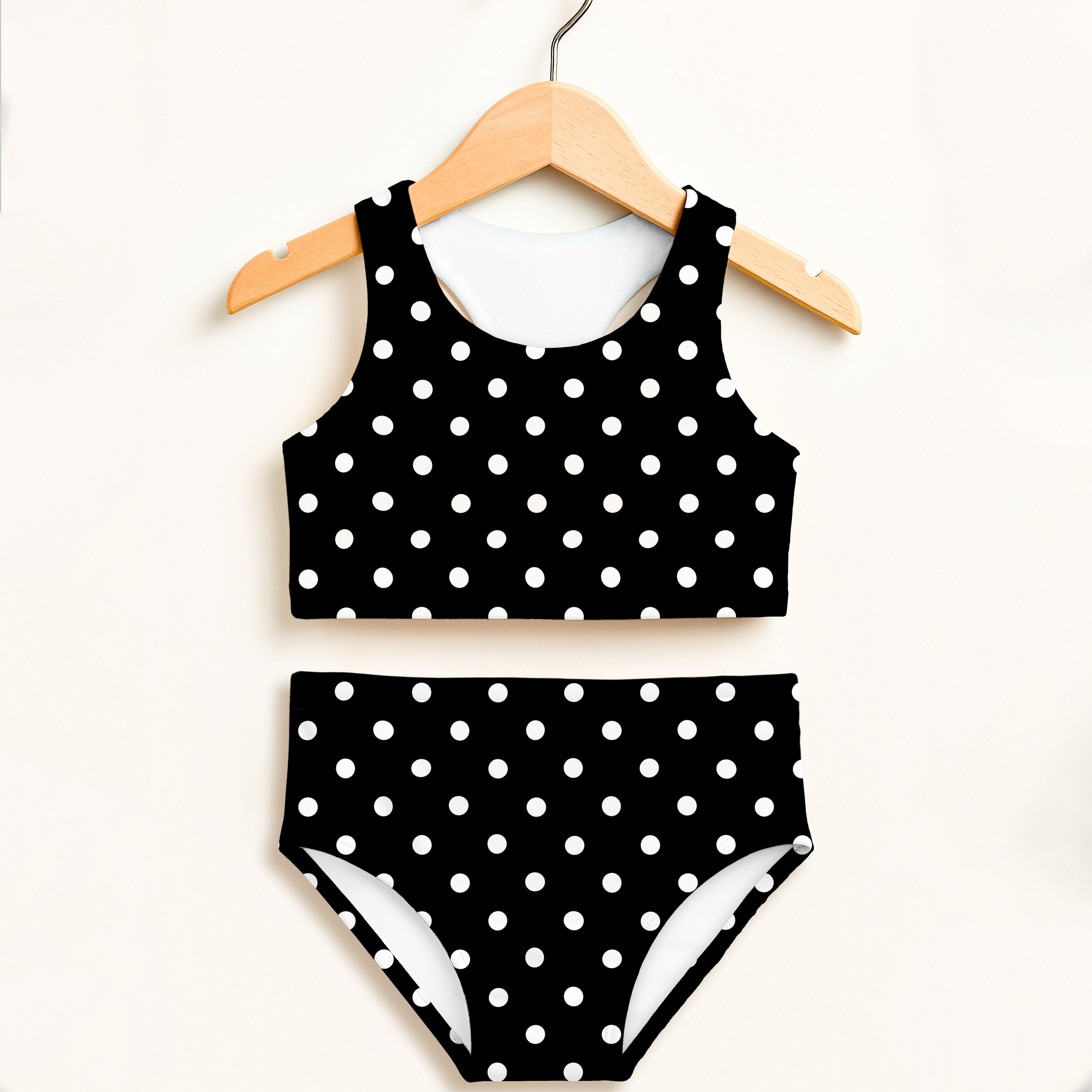 Girls black and white polka dot two-piece swimsuit with double layered fabric and high waist for sun protection hanging on wooden hanger