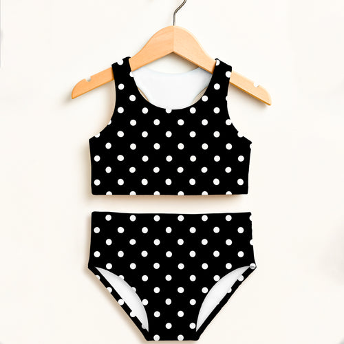 Girls black and white polka dot two-piece swimsuit with double layered fabric and high waist for sun protection hanging on wooden hanger