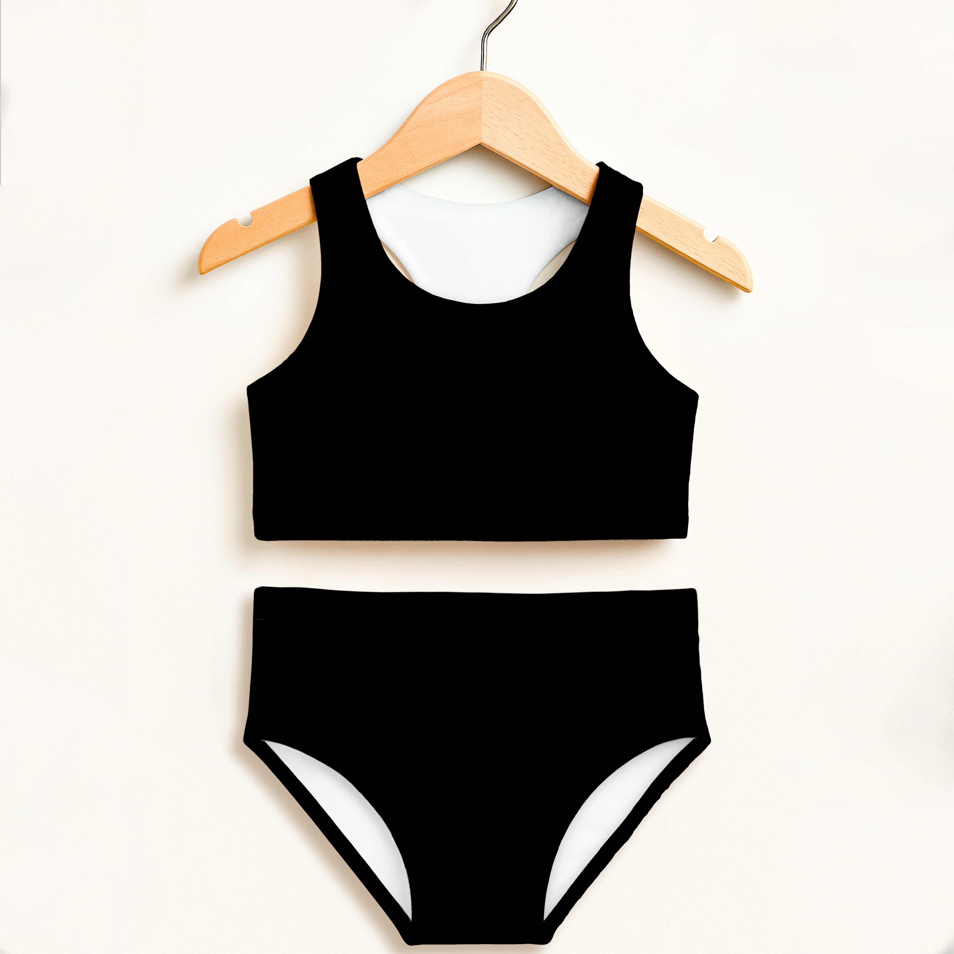 Girls black two piece swimsuit with white trim on bottoms hanging on wooden hanger featuring UPF 50+ high waisted comfort