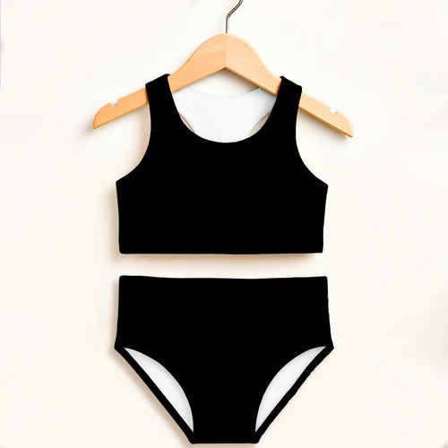 Girls black two piece swimsuit with white trim on bottoms hanging on wooden hanger featuring UPF 50+ high waisted comfort