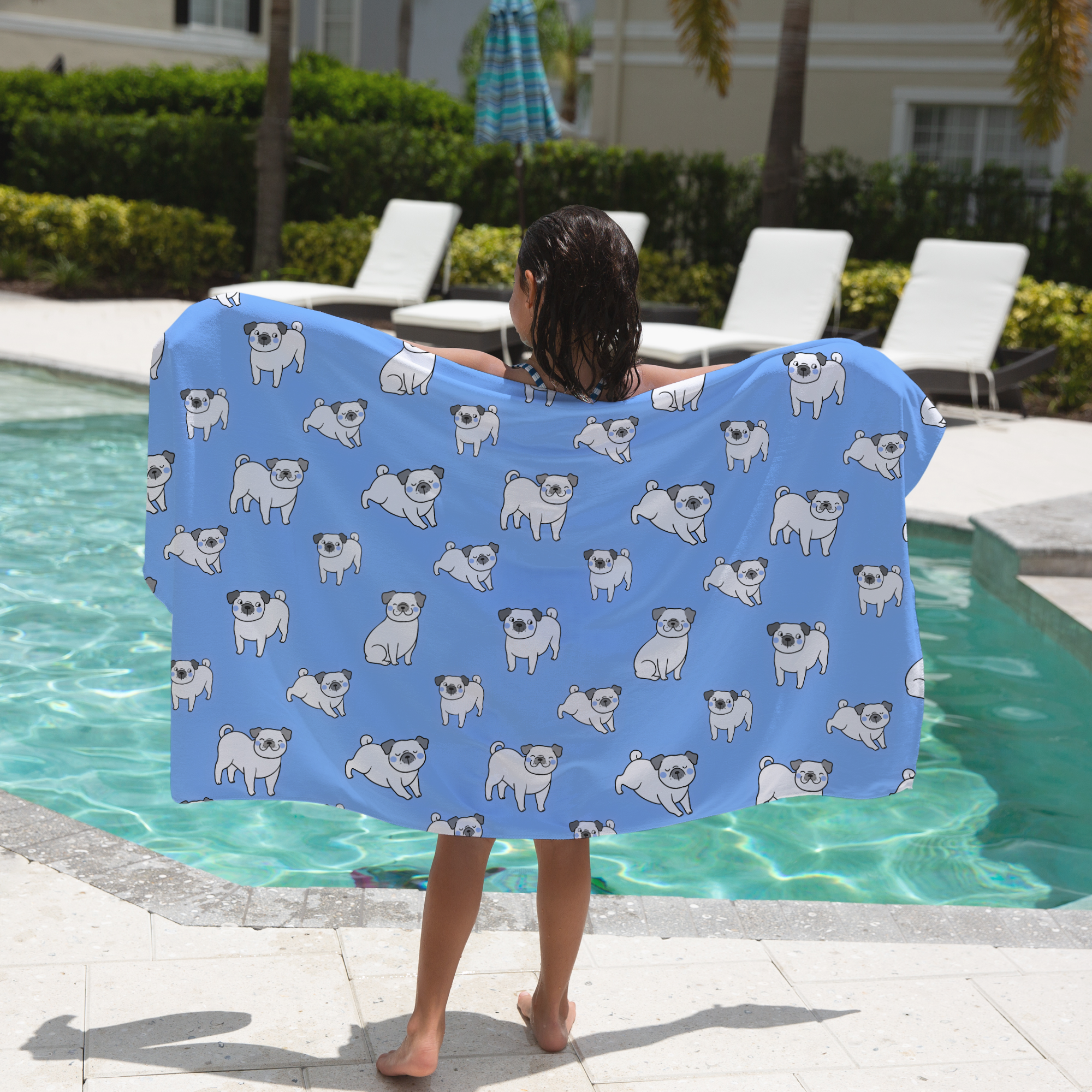 Child holding a blue towel with pug patterns by a pool