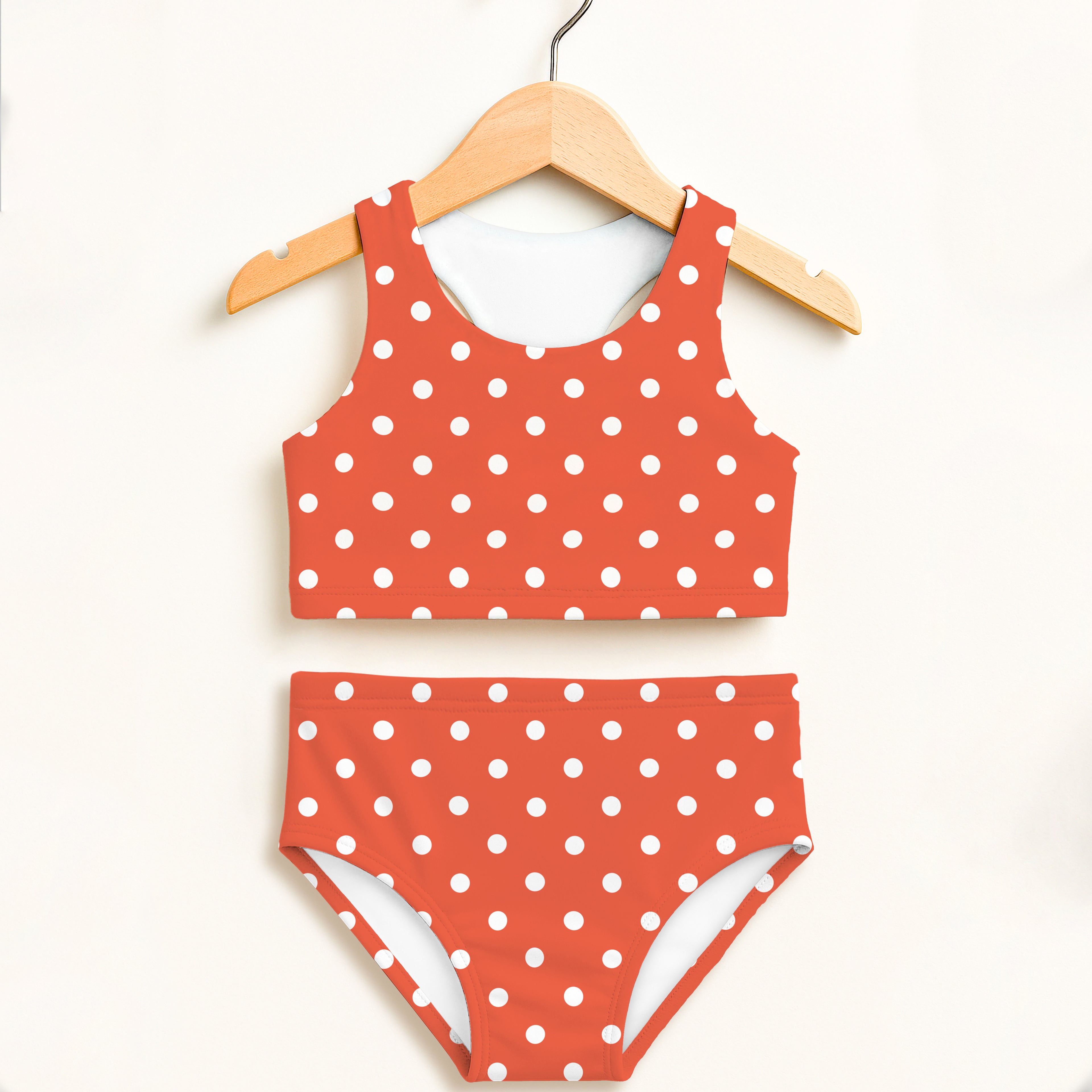 Girls bright orange and white polka dot two-piece swimsuit with double layered fabric and UPF 50+ sun protection hanging on wooden hanger
