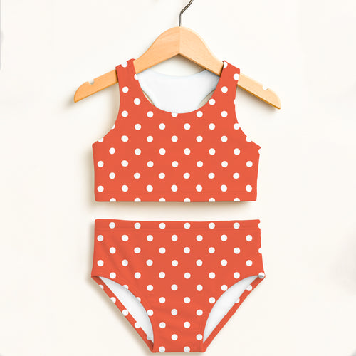 Girls bright orange and white polka dot two-piece swimsuit with double layered fabric and UPF 50+ sun protection hanging on wooden hanger