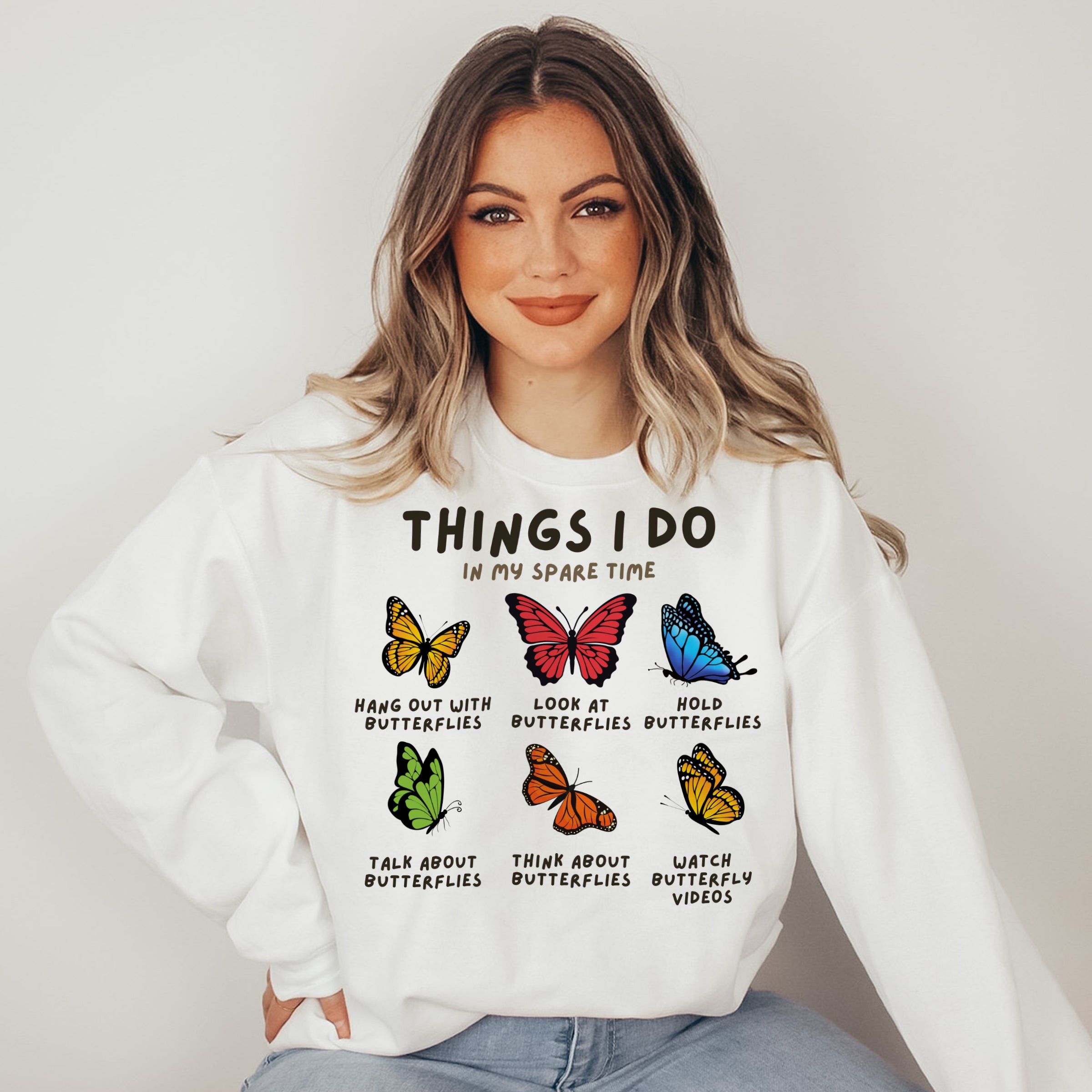Woman wearing a white sweatshirt with butterfly graphics and text.