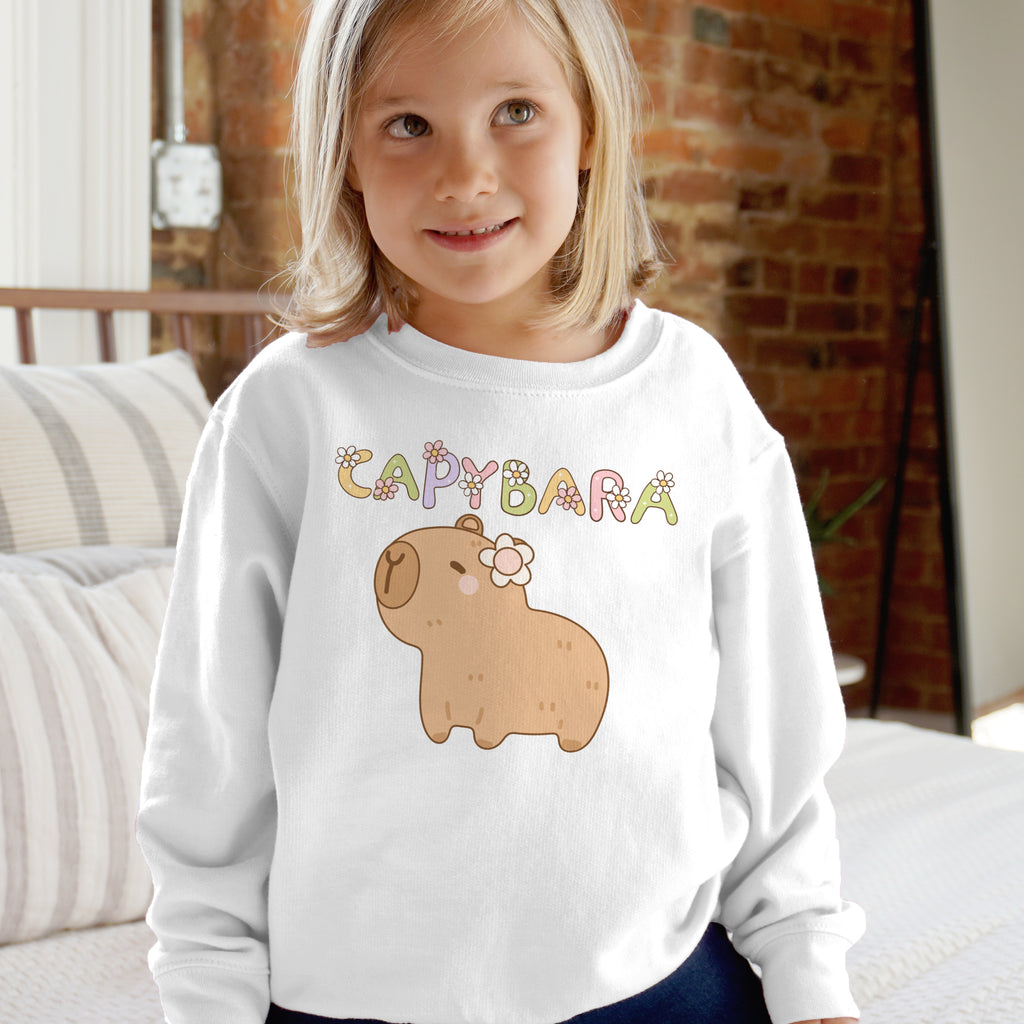Child wearing a white sweatshirt with a cartoon dog and 'Capybara' text in a home setting.