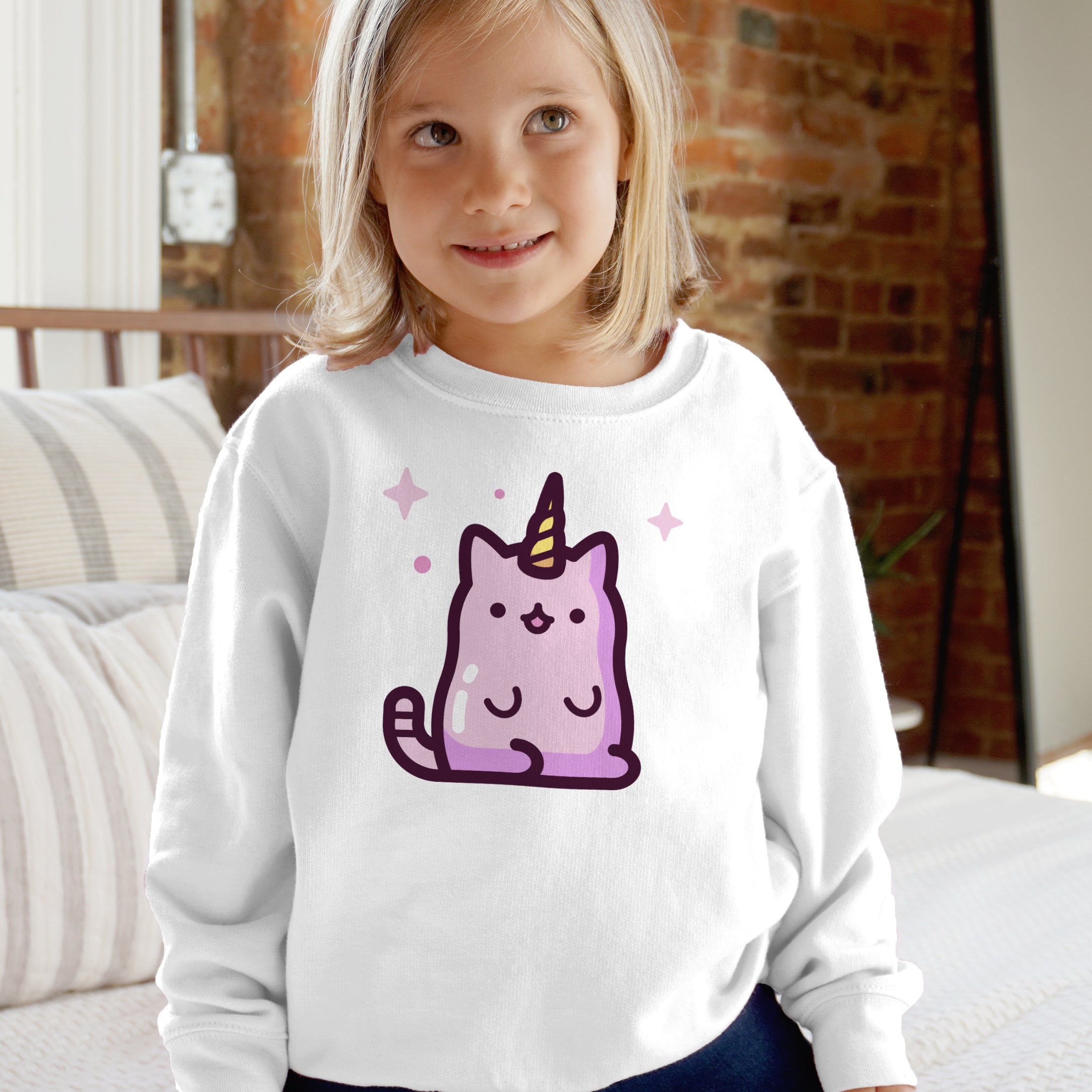 White long-sleeved kids sweatshirt featuring a purple caticorn with golden horn and pink sparkles on the front