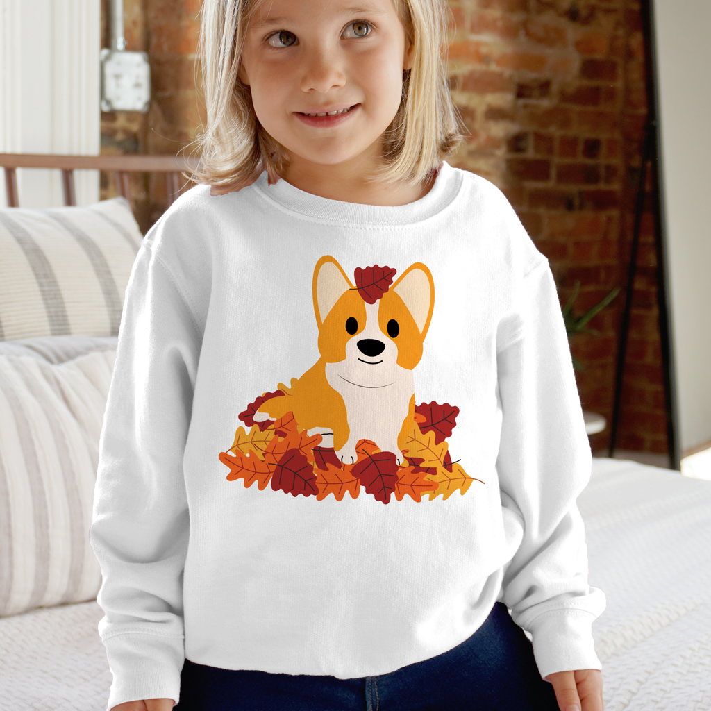 White long-sleeved kids sweatshirt featuring a cartoon corgi surrounded by orange and red autumn leaves