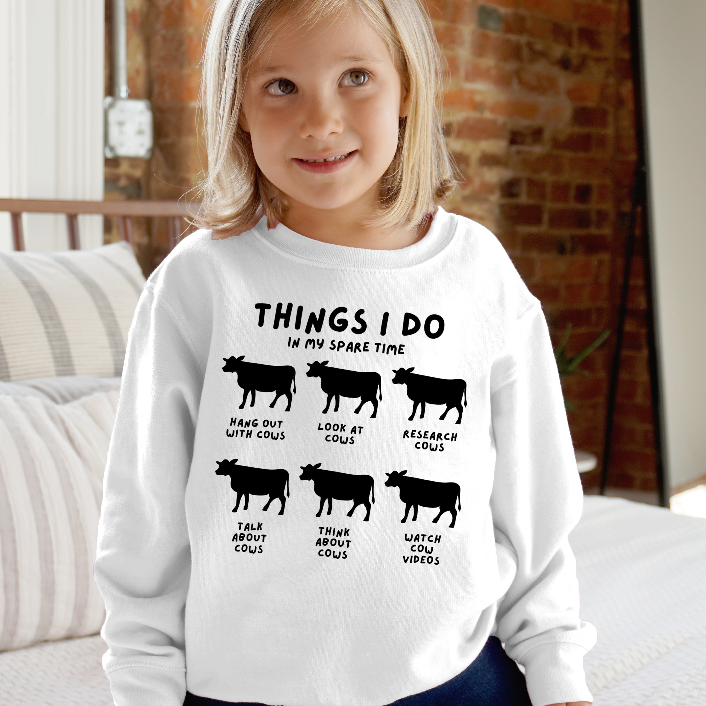 Child wearing a white sweatshirt with text and cow illustrations