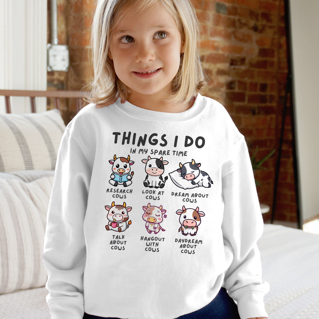Child wearing a white sweatshirt with cartoon cows and text in a casual indoor setting.
