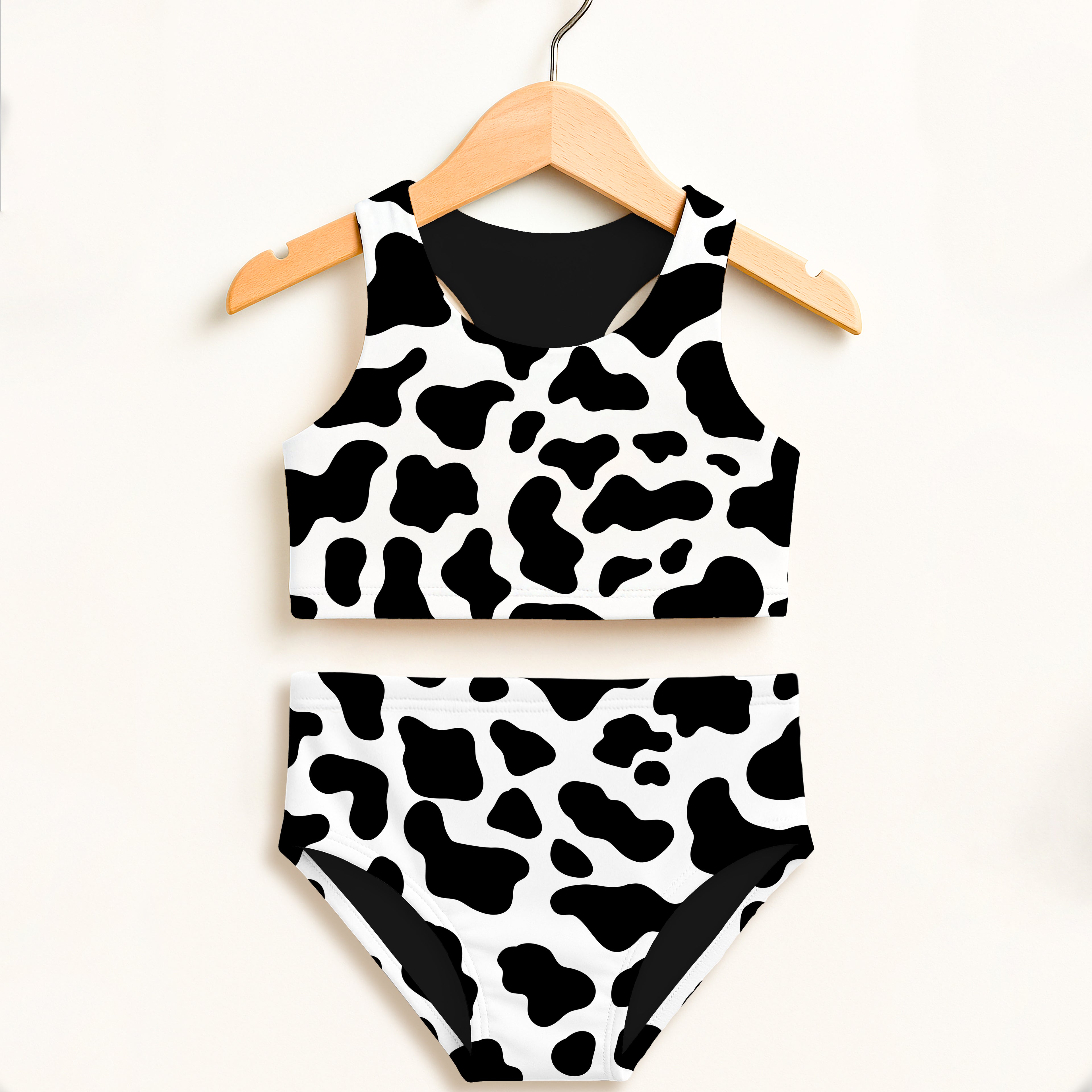 Girls cow print two piece swimsuit hanging on wooden hanger with black and white pattern and UPF 50 plus protection