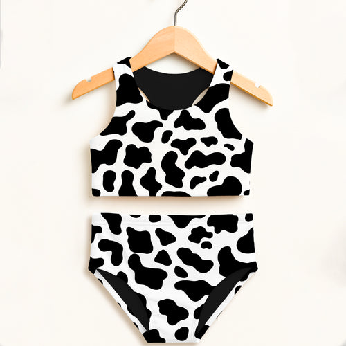 Girls cow print two piece swimsuit hanging on wooden hanger with black and white pattern and UPF 50 plus protection