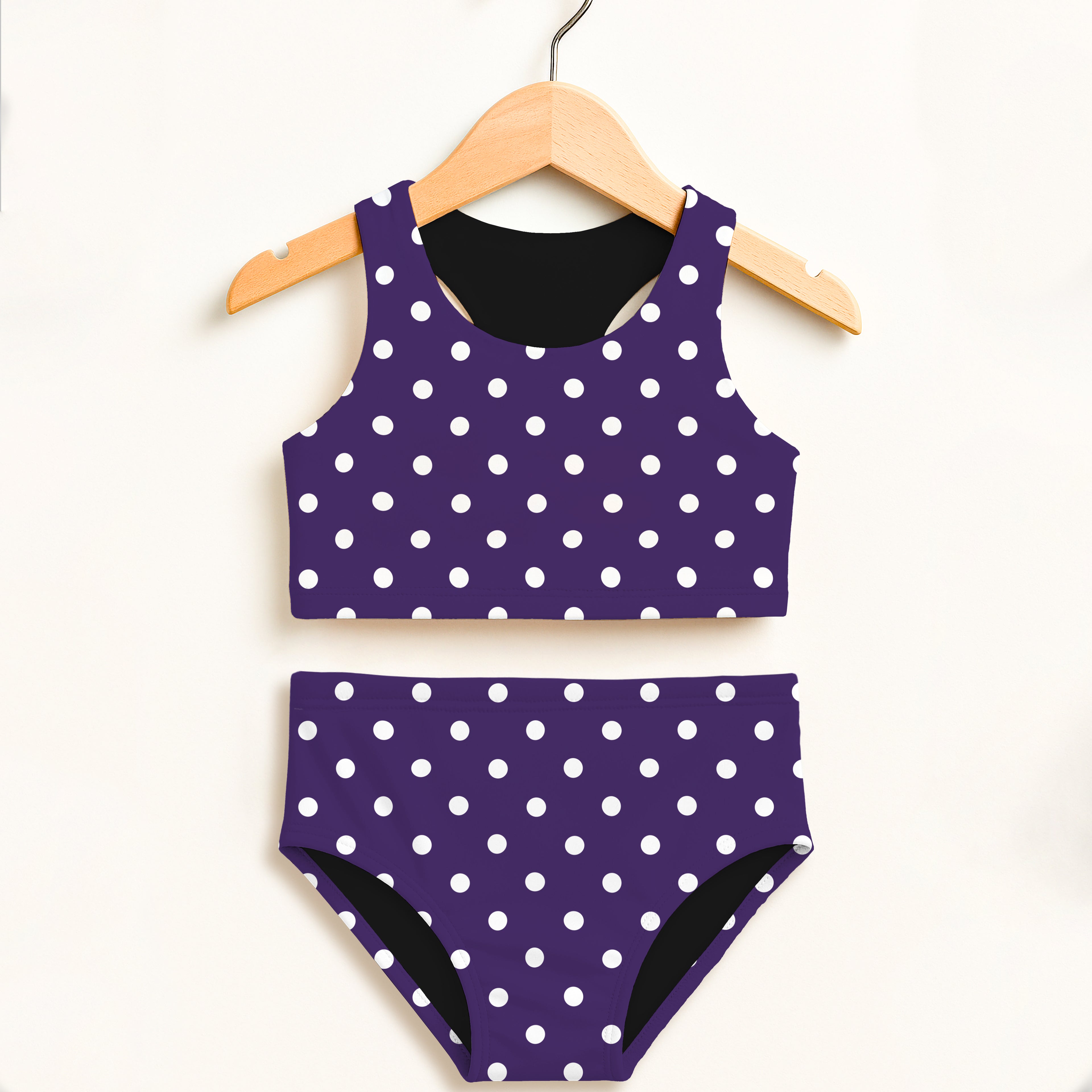 Girls dark purple polka dot two piece swimsuit with white dots and black lining hanging on wooden hanger