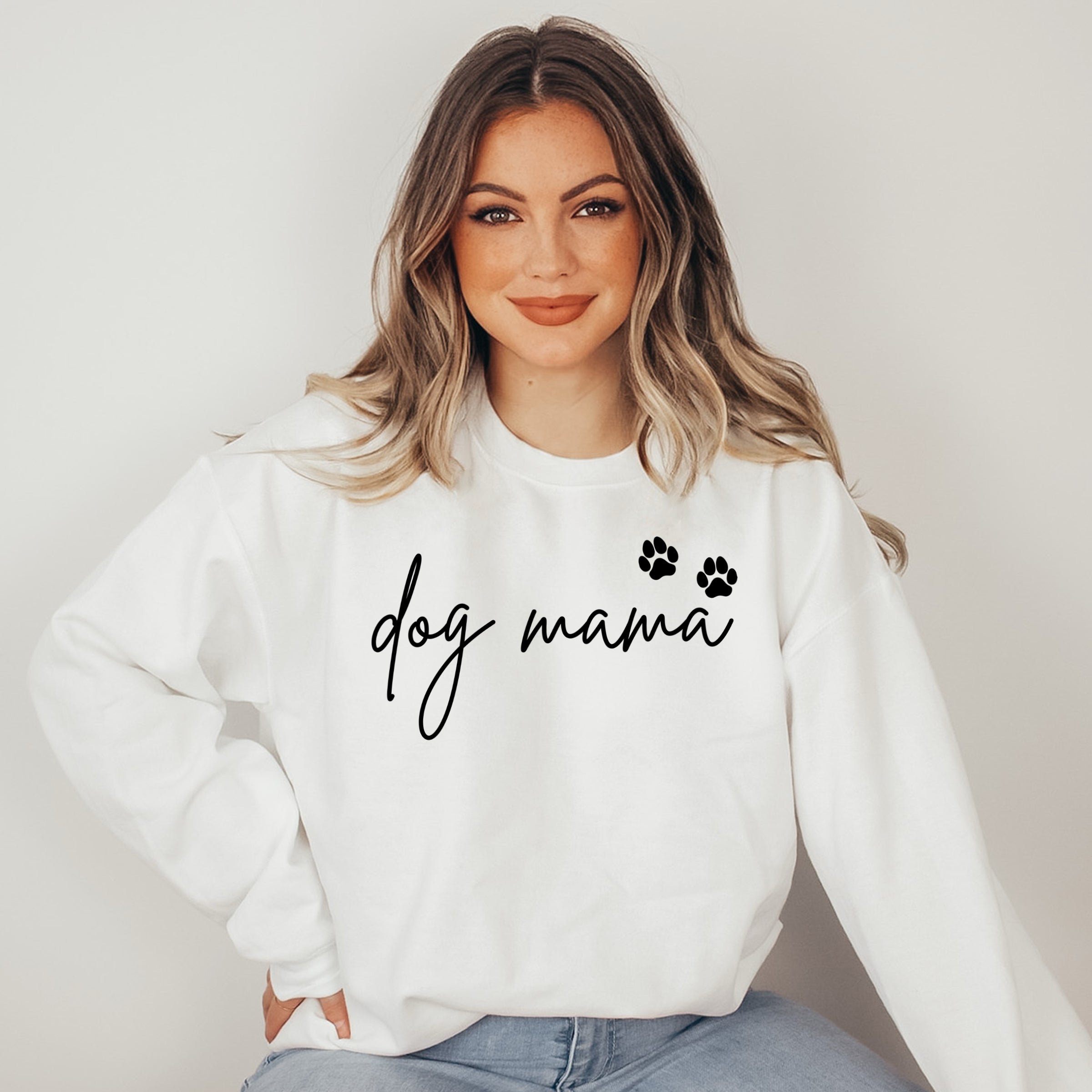Woman wearing a white sweatshirt with 'dog mama' text and paw prints on a plain background