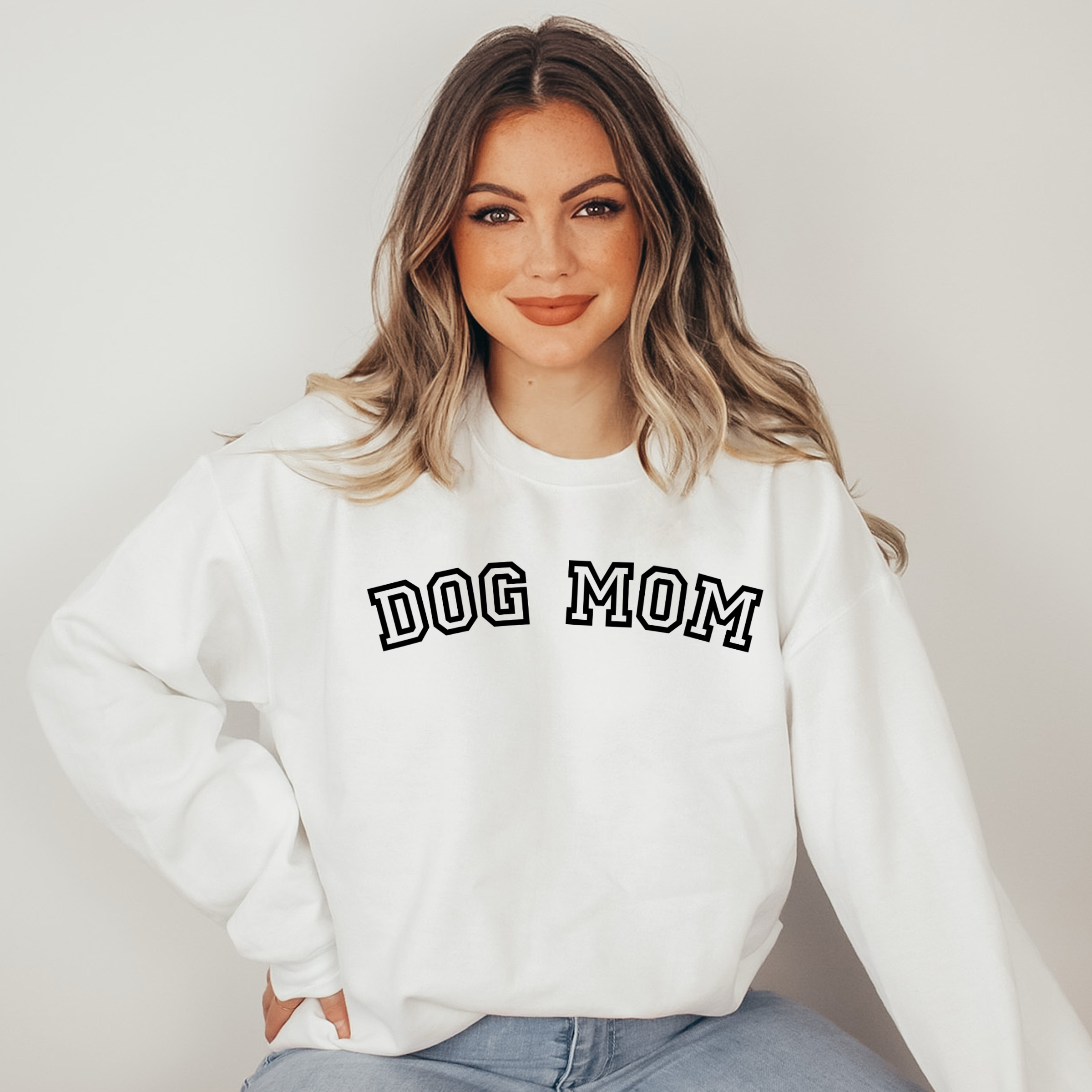 Woman wearing a white sweatshirt with 'DOG MOM' text on a plain background