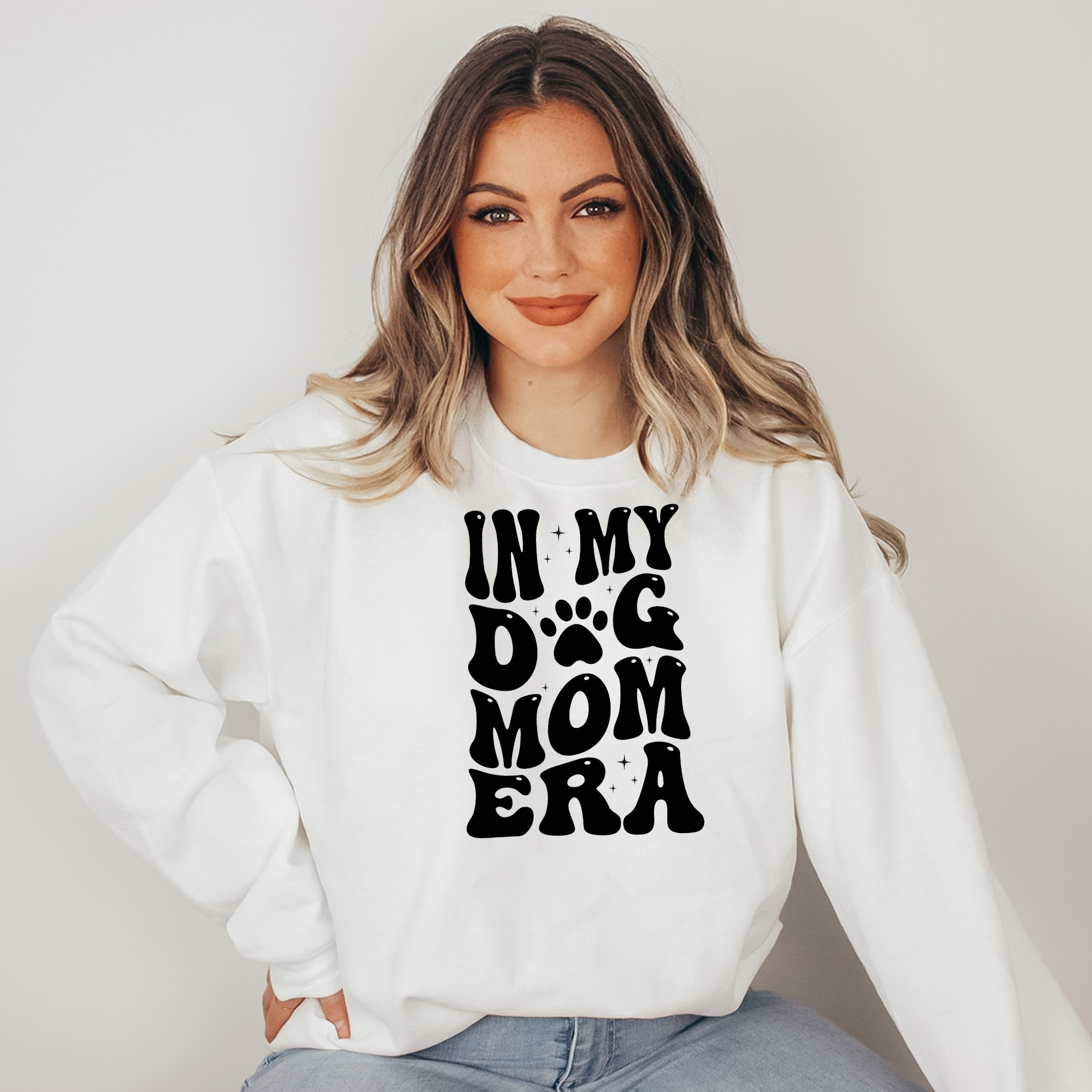 Woman wearing a white sweatshirt with 'IN MY DOG MOM ERA' text on a plain background