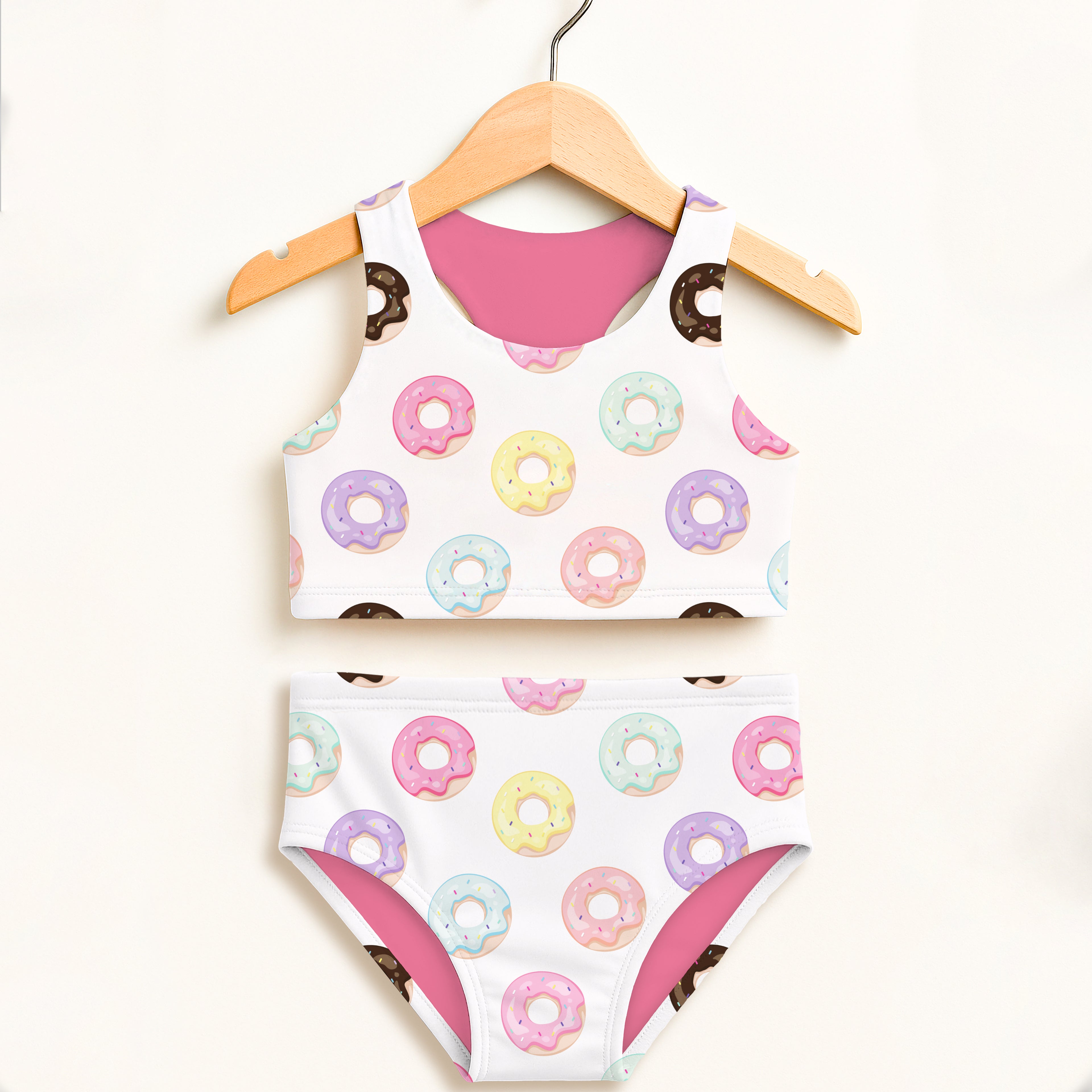 White girls two-piece swimsuit with colorful pastel donut pattern and pink lining on wooden hanger, upf 50+ comfort