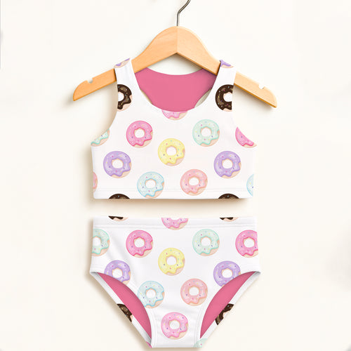 White girls two-piece swimsuit with colorful pastel donut pattern and pink lining on wooden hanger, upf 50+ comfort