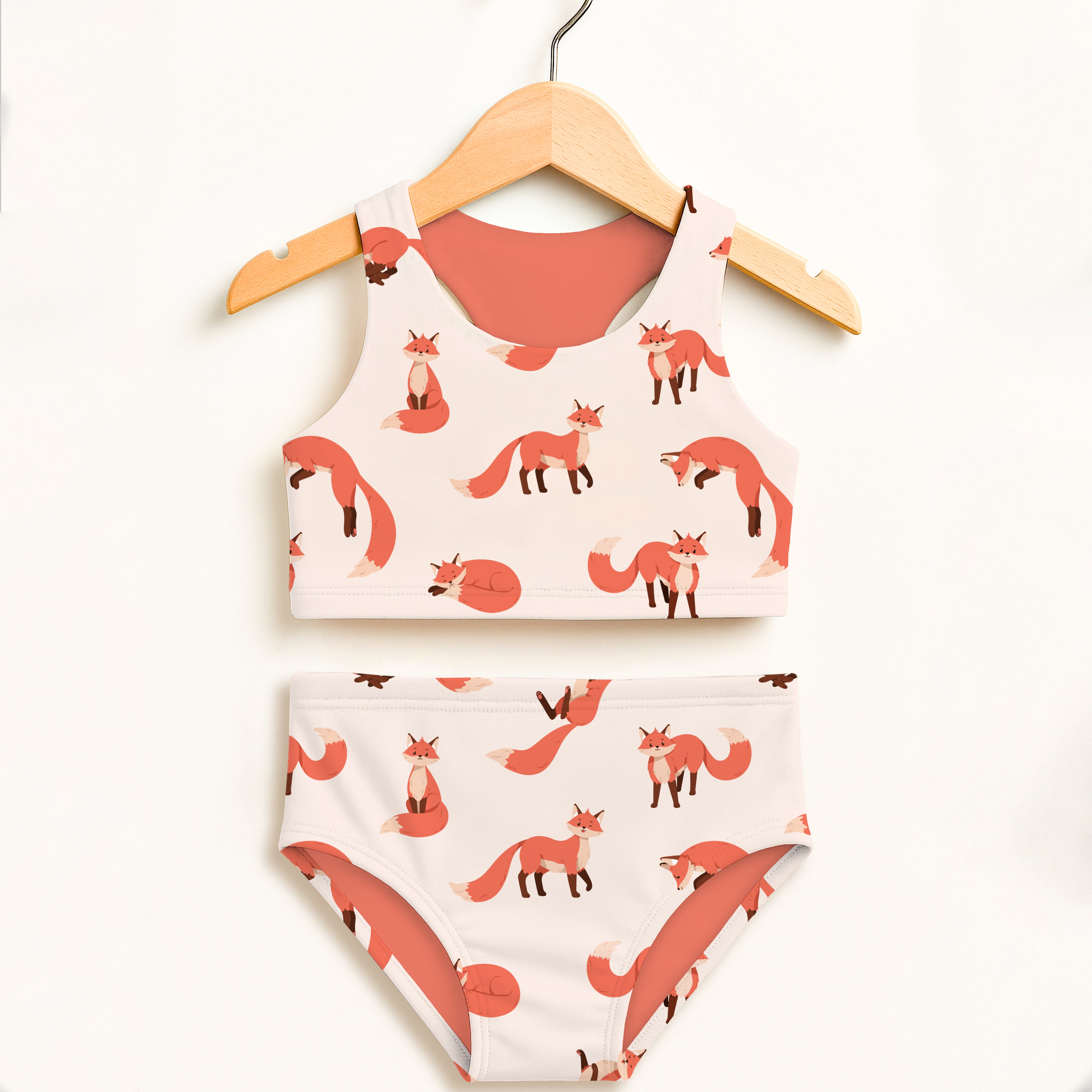 A girls fox two piece swimsuit with coral and cream fox print in double layered high waisted UPF 50 plus fabric on wooden hanger