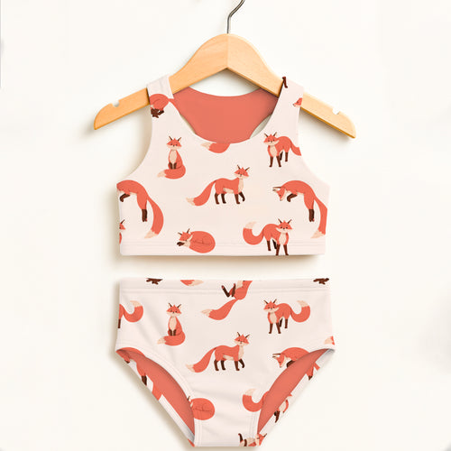 A girls fox two piece swimsuit with coral and cream fox print in double layered high waisted UPF 50 plus fabric on wooden hanger