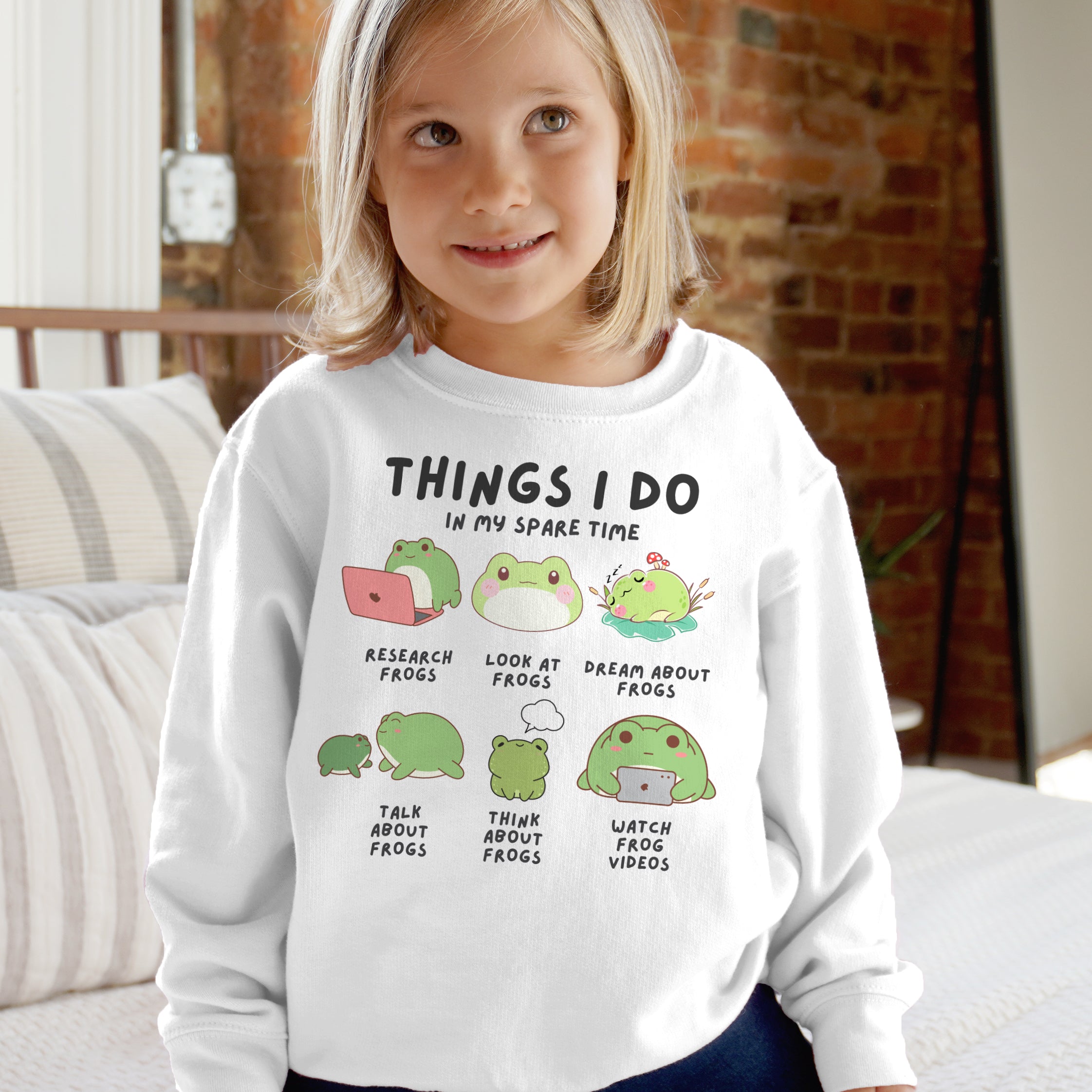 Child wearing a white sweatshirt with frog-themed text and graphics