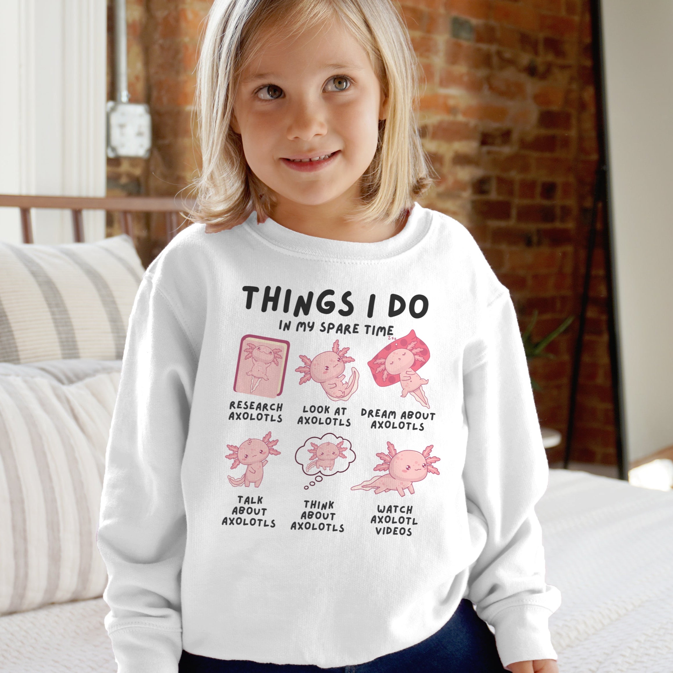 Child wearing a white sweatshirt with axolotl-themed graphics and text.